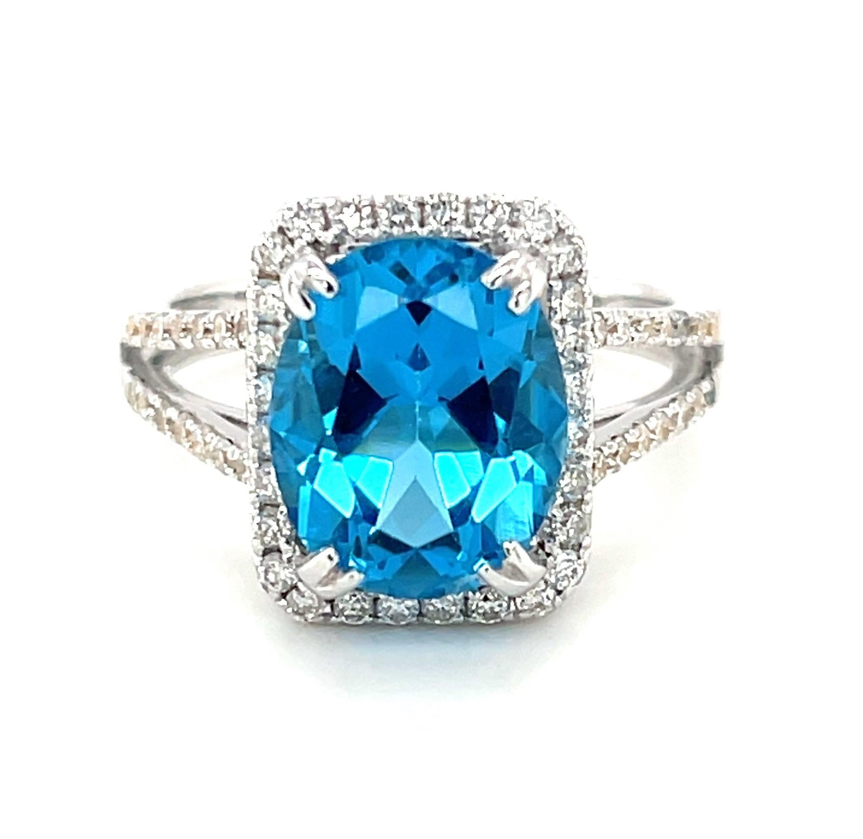 This sparkling cocktail ring features a beautiful 4.38 carat bright  blue topaz oval surrounded by a diamond halo set in 18k white gold. The rectangular halo gives the ring a modern look and shows off the beautiful shape of the center gem. Brilliant