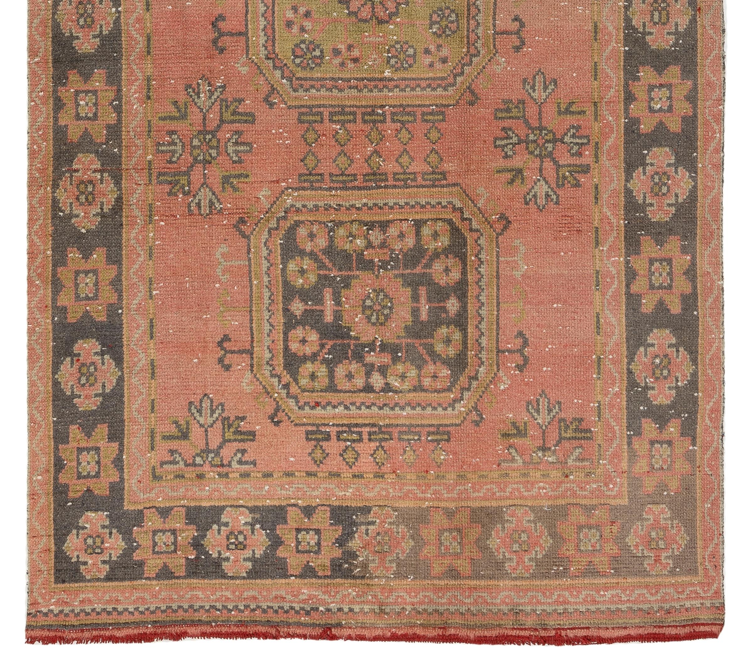 A vintage Turkish runner rug, hand-knotted with low wool pile on cotton foundation. It features linked rectilinear medallions decorated with floral head motifs against a field in dark coral pink. It is in good condition, professionally-washed,