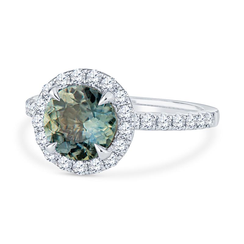 This diamond halo ring features an uncommon 1.40 carat round, no heat, teal color shifting sapphire surrounded by 0.54 carat total weight in round diamonds set in 18 karat white gold. This ring is a size 5.5 but can be resized upon request.