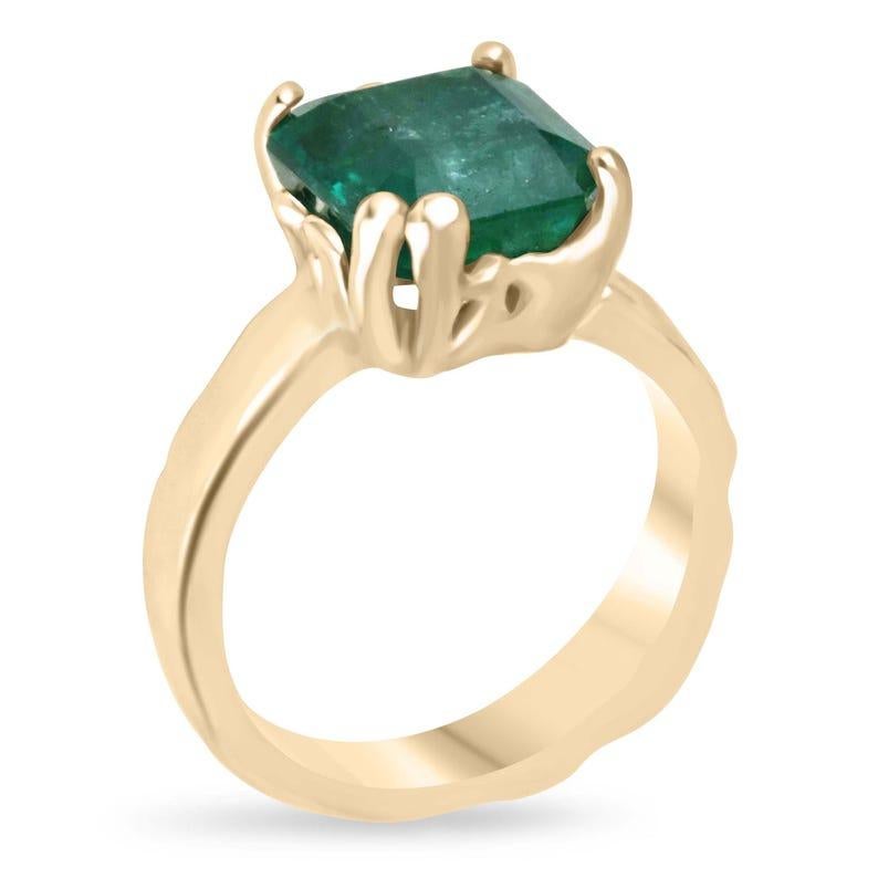 This captivating solitaire ring features an Asscher-cut Zambian emerald, boasting a rich dark green color with semi-transparent clarity. Set in a fun, organic gold design, the intricate prongs and gold nugget-like band style add a unique, earthy