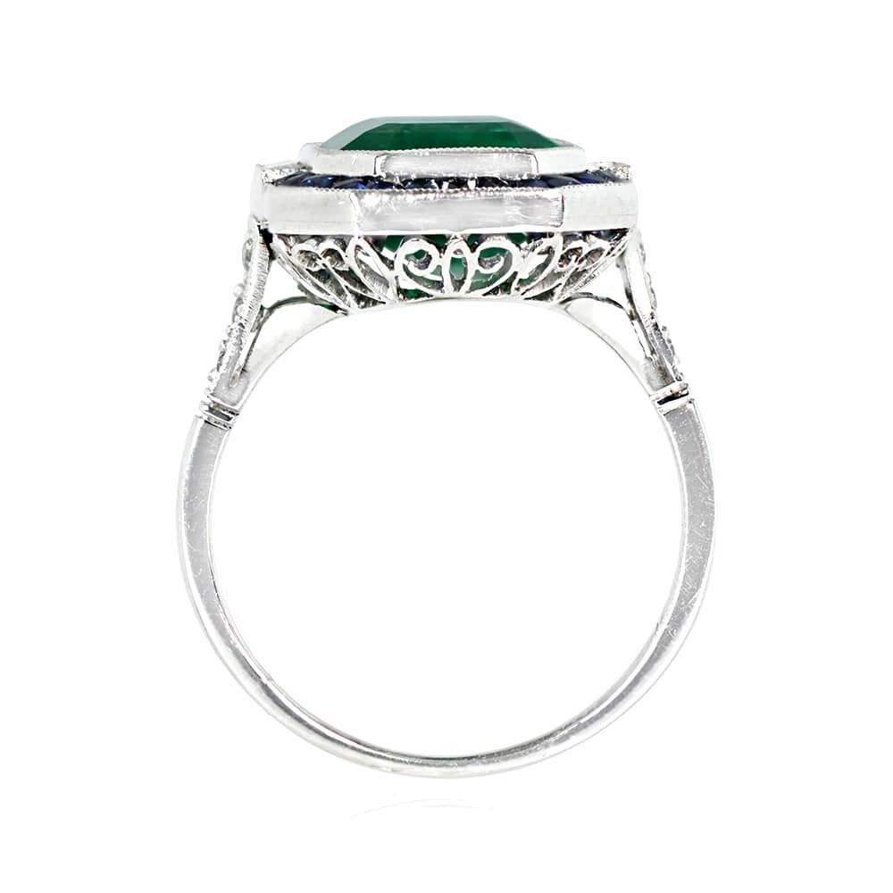 This gemstone ring has a 4.49-carat natural Colombian emerald at its center, accented by baguette-cut diamonds and a French-cut sapphire halo. The total sapphire weight is around 0.78 carats, and there are single-cut diamonds along the shoulders,