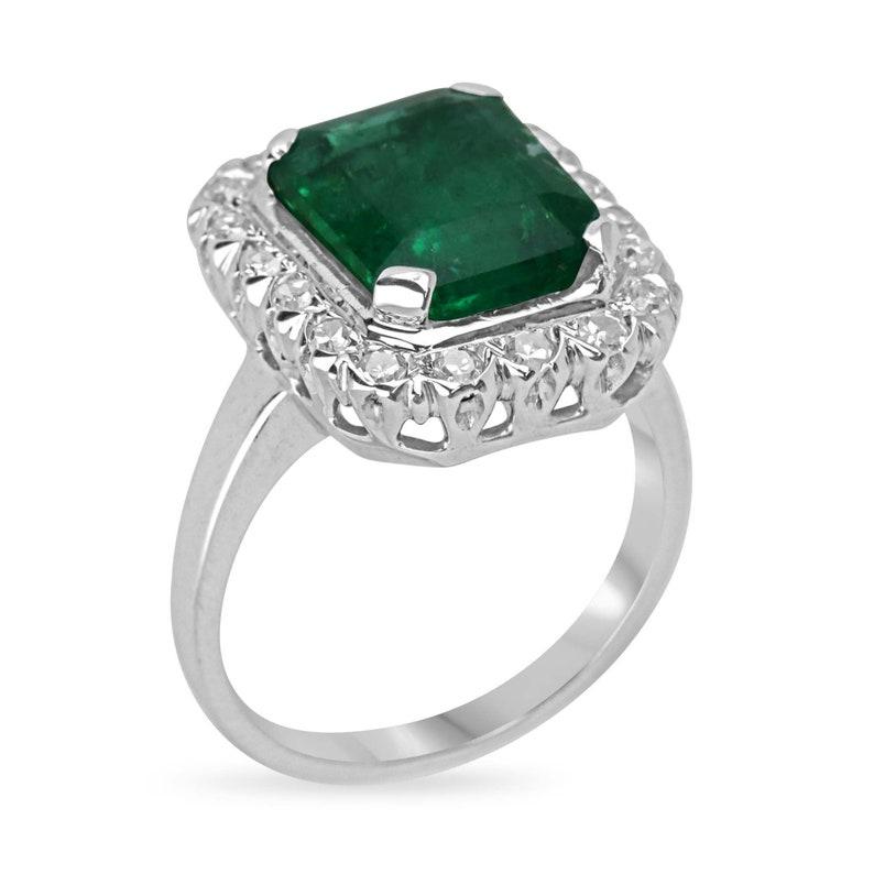 Declare your love with timeless elegance through our Emerald and Diamond Halo Engagement Ring. Featuring a resplendent emerald boasting over 4 carats of lush, dark green brilliance, this enchanting gem is set vertically, commanding attention. The
