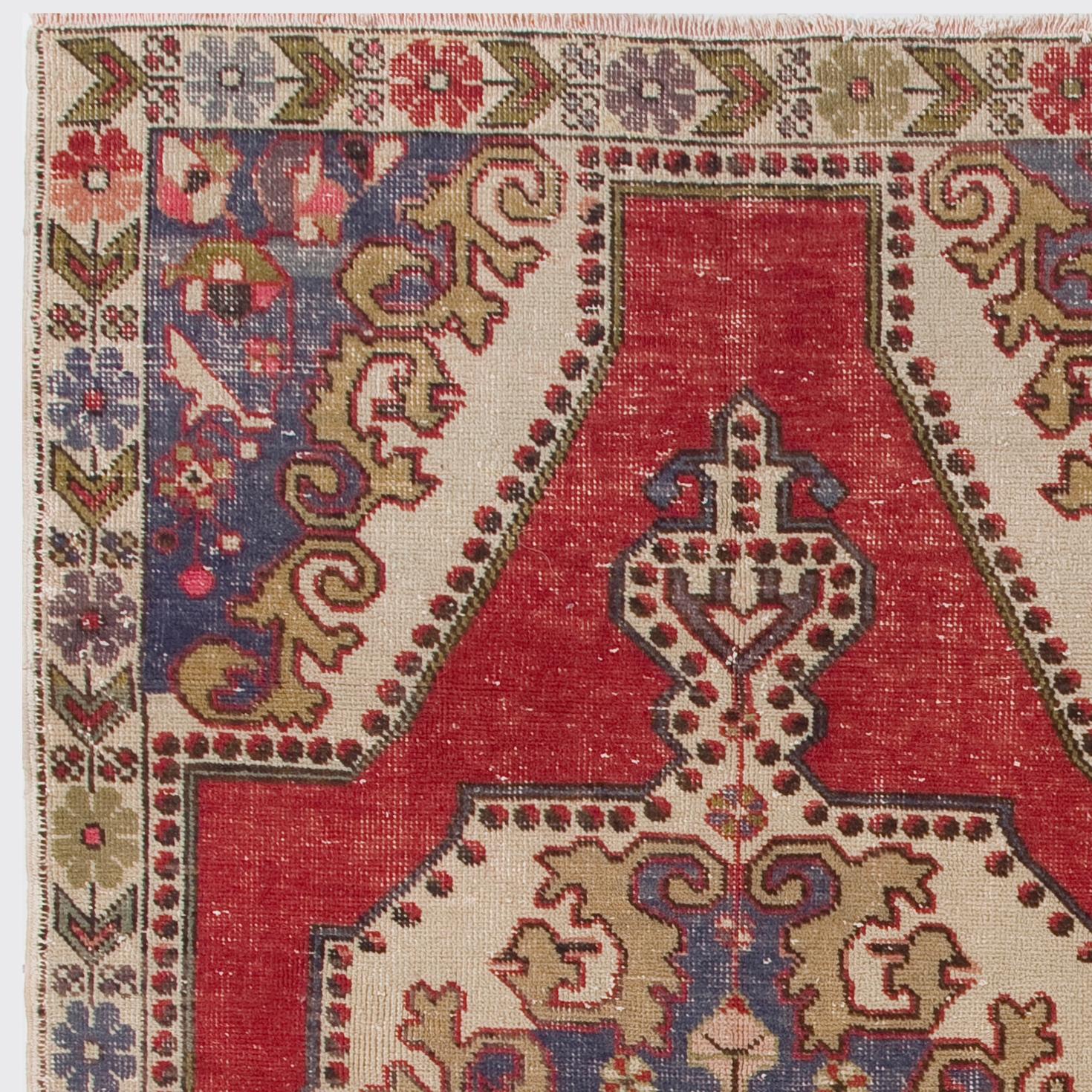 A vintage hand knotted Turkish area rug featuring a large medallion design in ivory at the centre of a key-hole shaped red field. The corner pieces are in ivory and blue and adorned with florals and large swirling leaves. There are navy and red