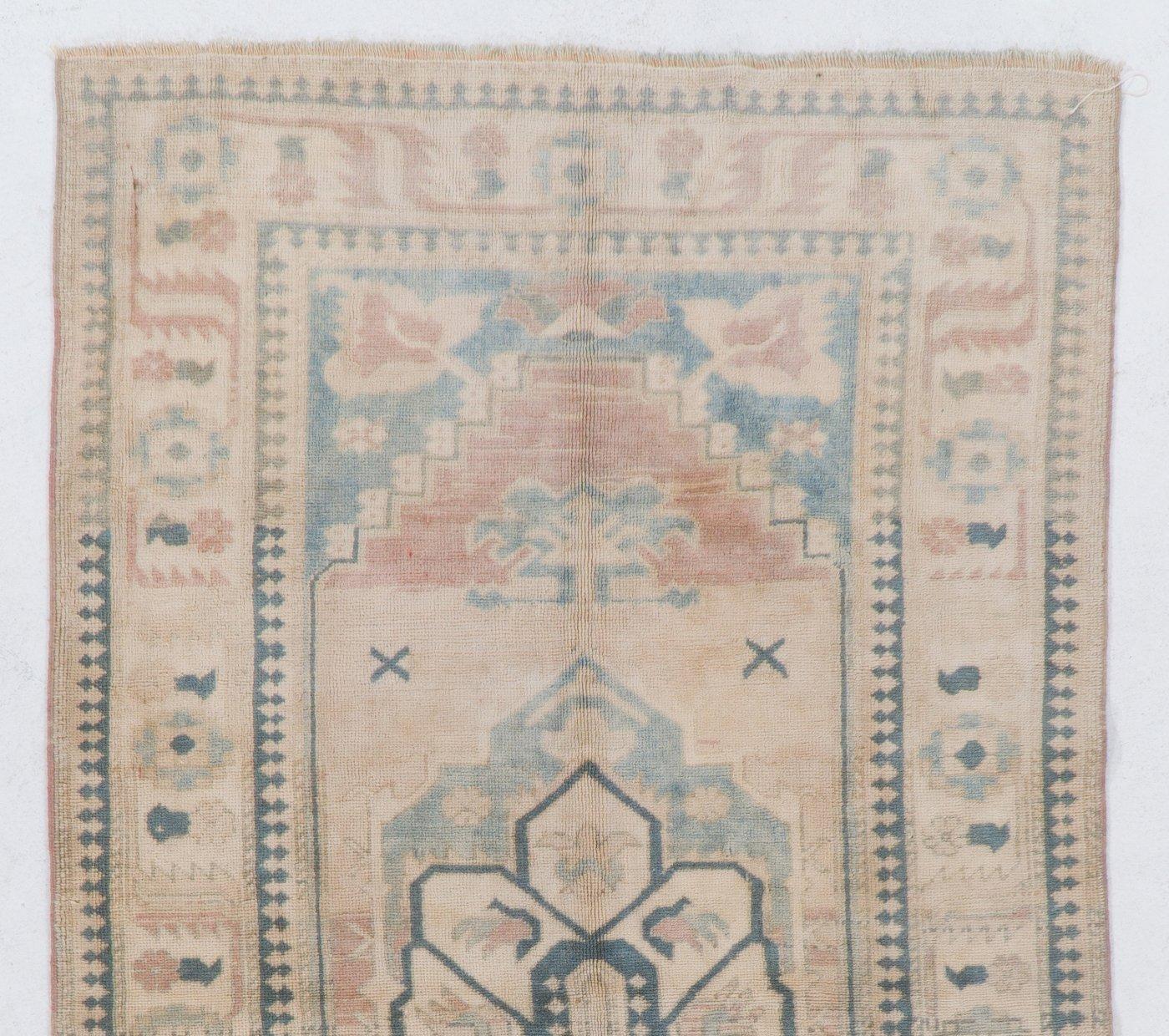 Hand-knotted vintage Turkish area rug with even medium wool pile on wool foundation and a design of a central geometric medallion and stylized florals and leaves in faded pink and blue colors. The rug is in very good condition, professionally