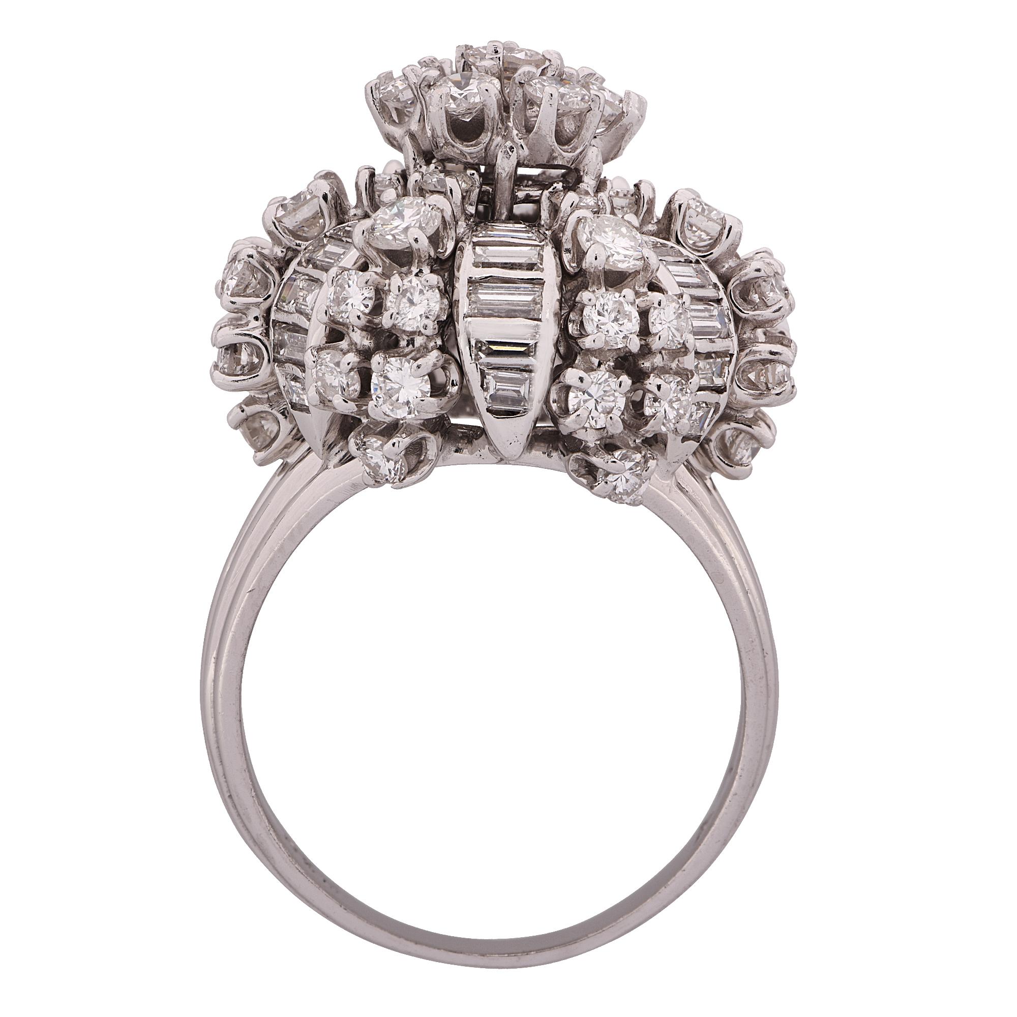 Bombe ring crafted in platinum, featuring approximately 4.5 carats total of round brilliant cut and baguette cut diamonds, G color VS clarity. A dainty flower crafted from 7 round brilliant cut diamonds rests in the center of the ring. Diamond rays