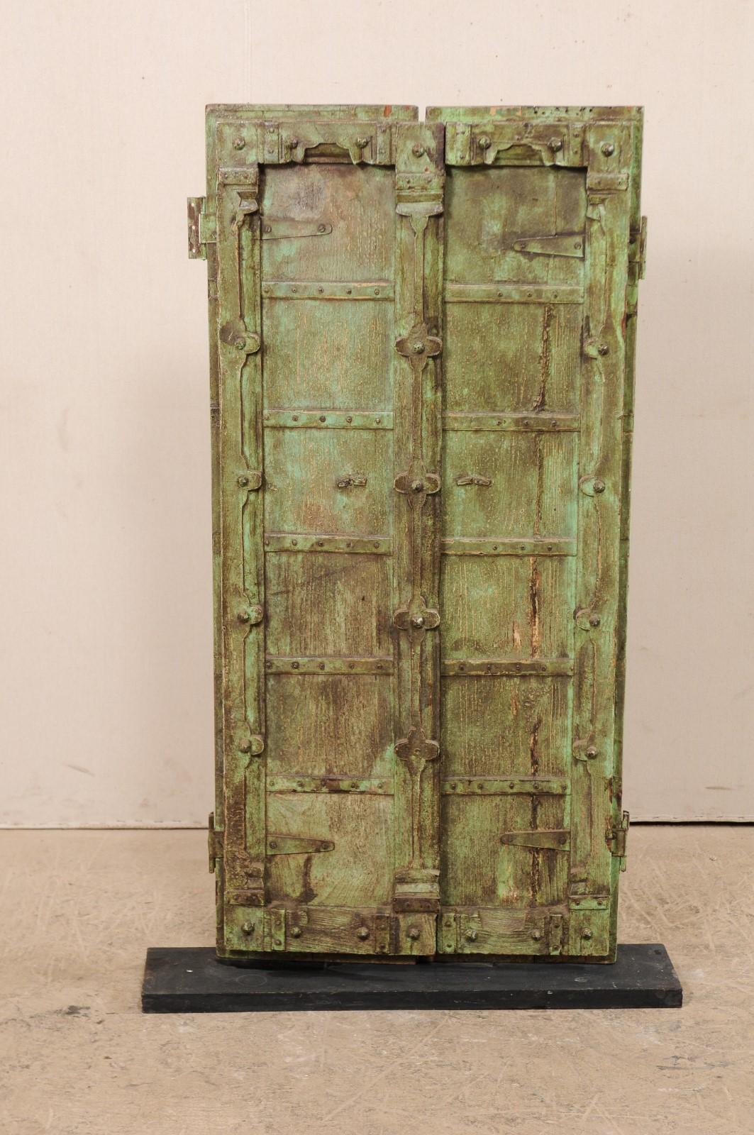 A short pair of Indian doors from the turn of the 19th and 20th centuries presented upon a custom Stand. This antique pair of doors each feature six vertically square panels, with sweetly carved flower motifs down the center where they meet as well