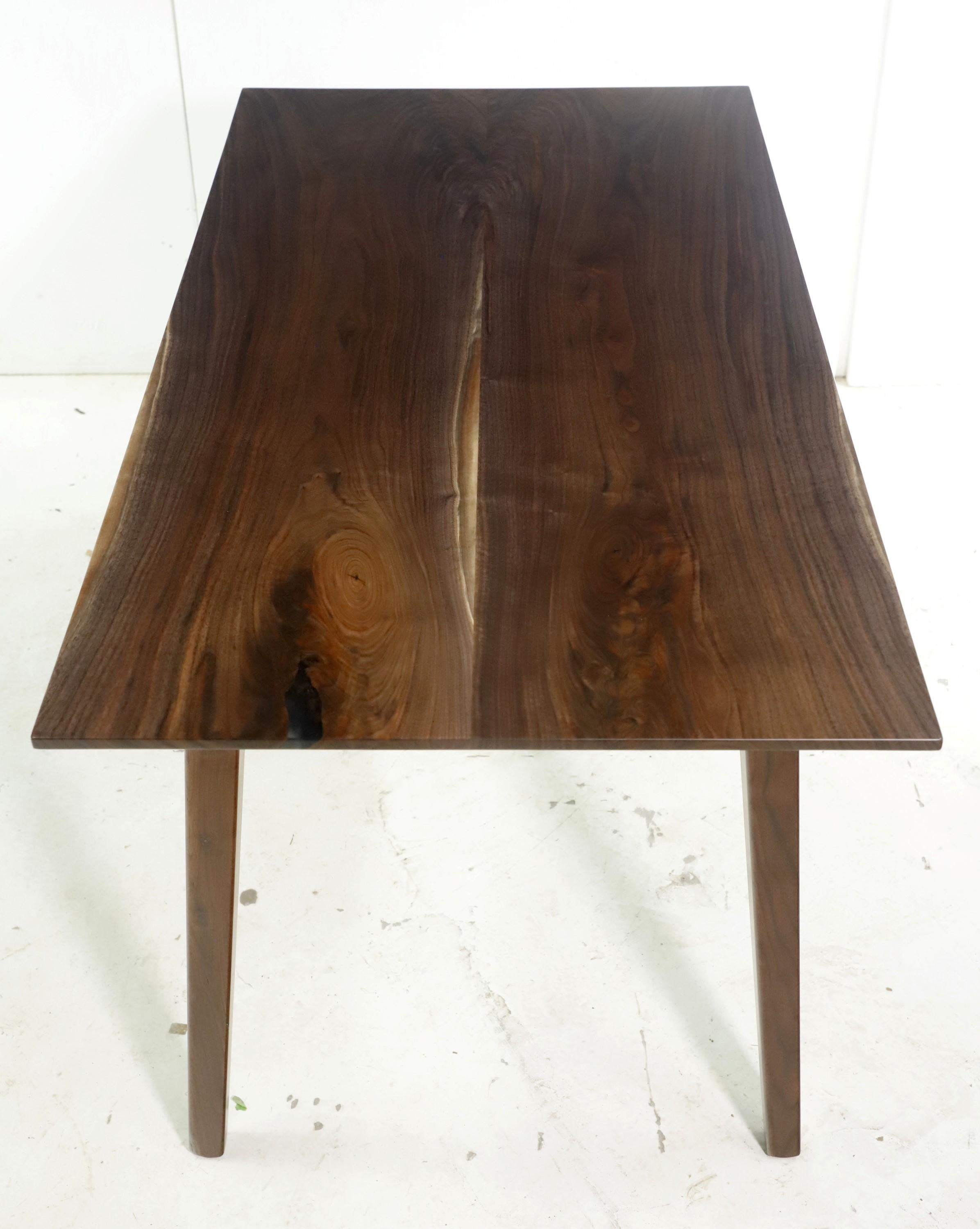 This table features a two slab solid walnut top with subtle small clear resin details pours down the center paired with tapered legs. This table is ready to ship. Please note, this item is located in our Scranton, PA location.
