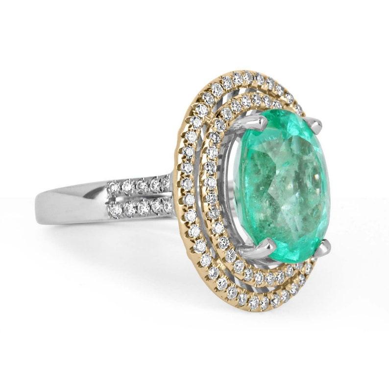 Este es un exquisito anillo colombiano de esmeralda y diamantes. El precioso engaste presenta una exquisita esmeralda ovalada de bello color y muy buena claridad ocular para su gran tamaño. Los diamantes casi incoloros forman un halo doble alrededor