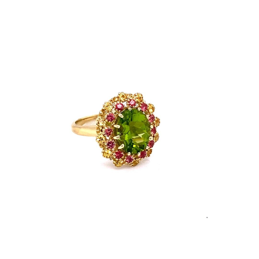 This beautiful ring has an Oval Cut Peridot that weighs 3.49 Carats and measures at 10 mm x 12 mm. The ring is surrounded by 24 Red and Yellow Sapphires that weigh 1.02 Carats. The total carat weight of this ring is 4.51 Carats. 
Curated in 14 Karat
