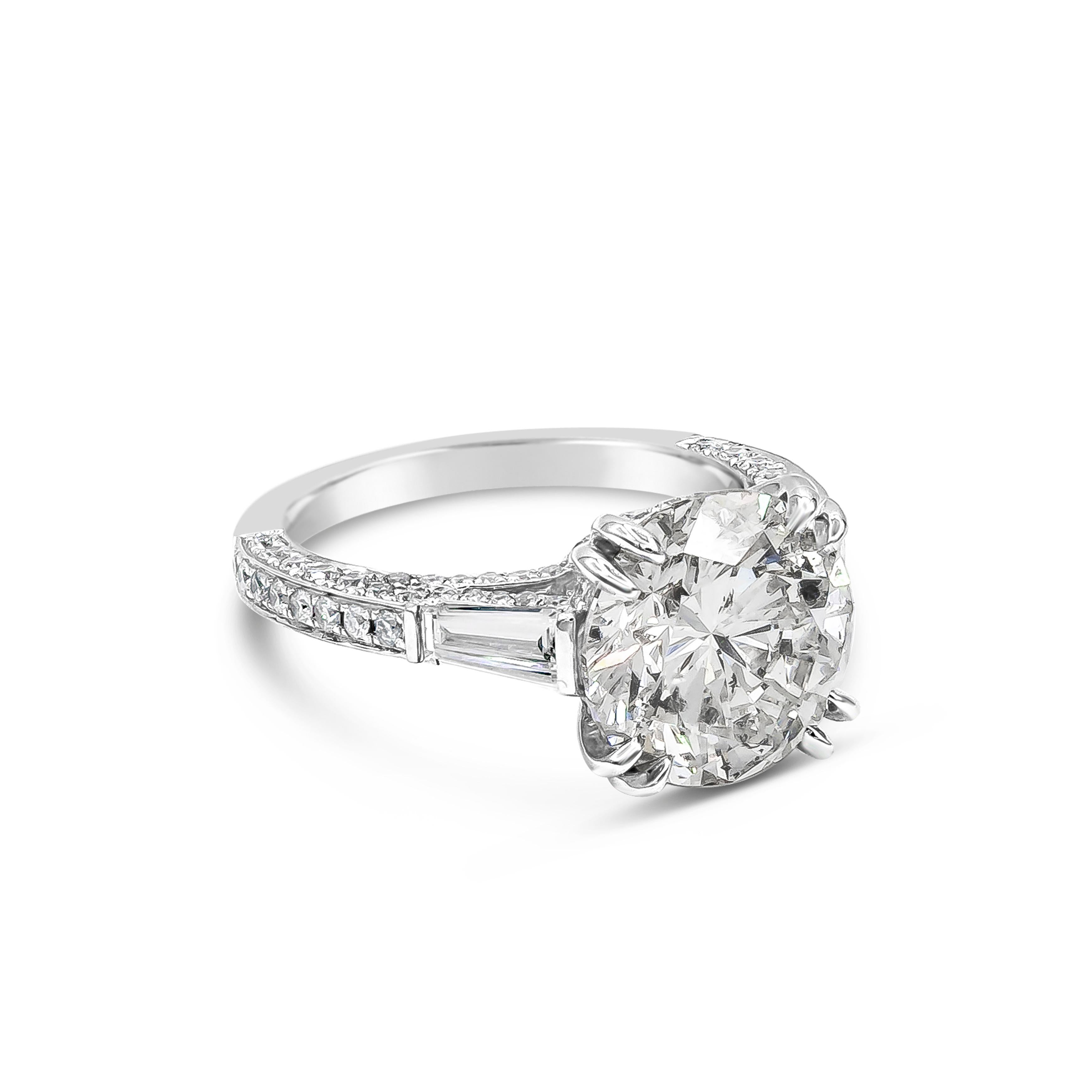 This gorgeous three stone engagement ring features a 4.53 carats brilliant round cut diamond certified by EGL as E color and SI2 in clarity, set in an eight prong basket setting. Flanked by tapered baguette diamonds on either side and accented with