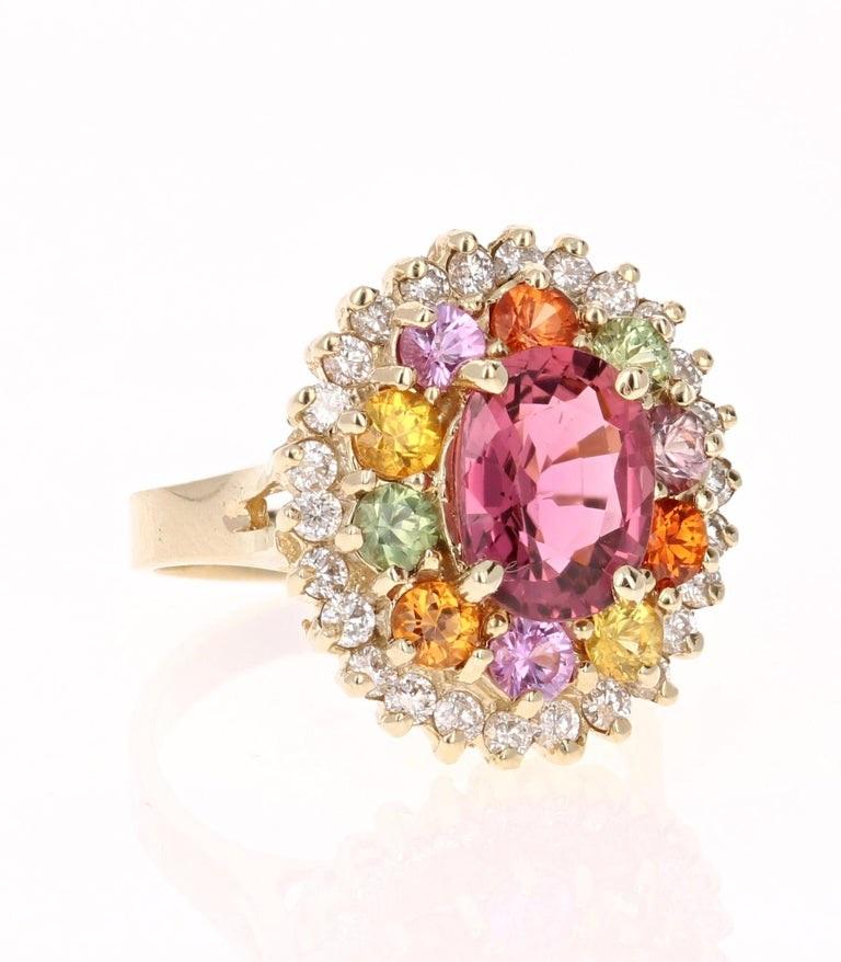 Dieser Ring hat einen 2,31 Karat Oval Cut Pinkish-Mauve Turmalin und ist elegant umgeben von 10 Round Cut Multi-Colored Sapphires, die 1,57 Karat wiegen und weiter von 26 Round Cut Diamanten, die 0,65 Karat wiegen umgeben. Das Gesamtkaratgewicht