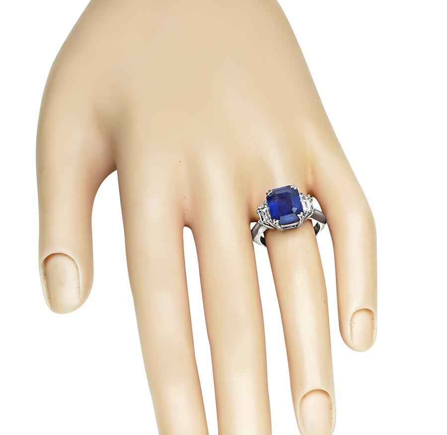 This is an elegant platinum engagement ring. The ring is centered with lovely emerald cut Ceylon sapphire that weighs approximately 4.56ct. The sapphire is accentuated by sparkling emerald cut diamonds that weigh approximately 0.90ct. The color of