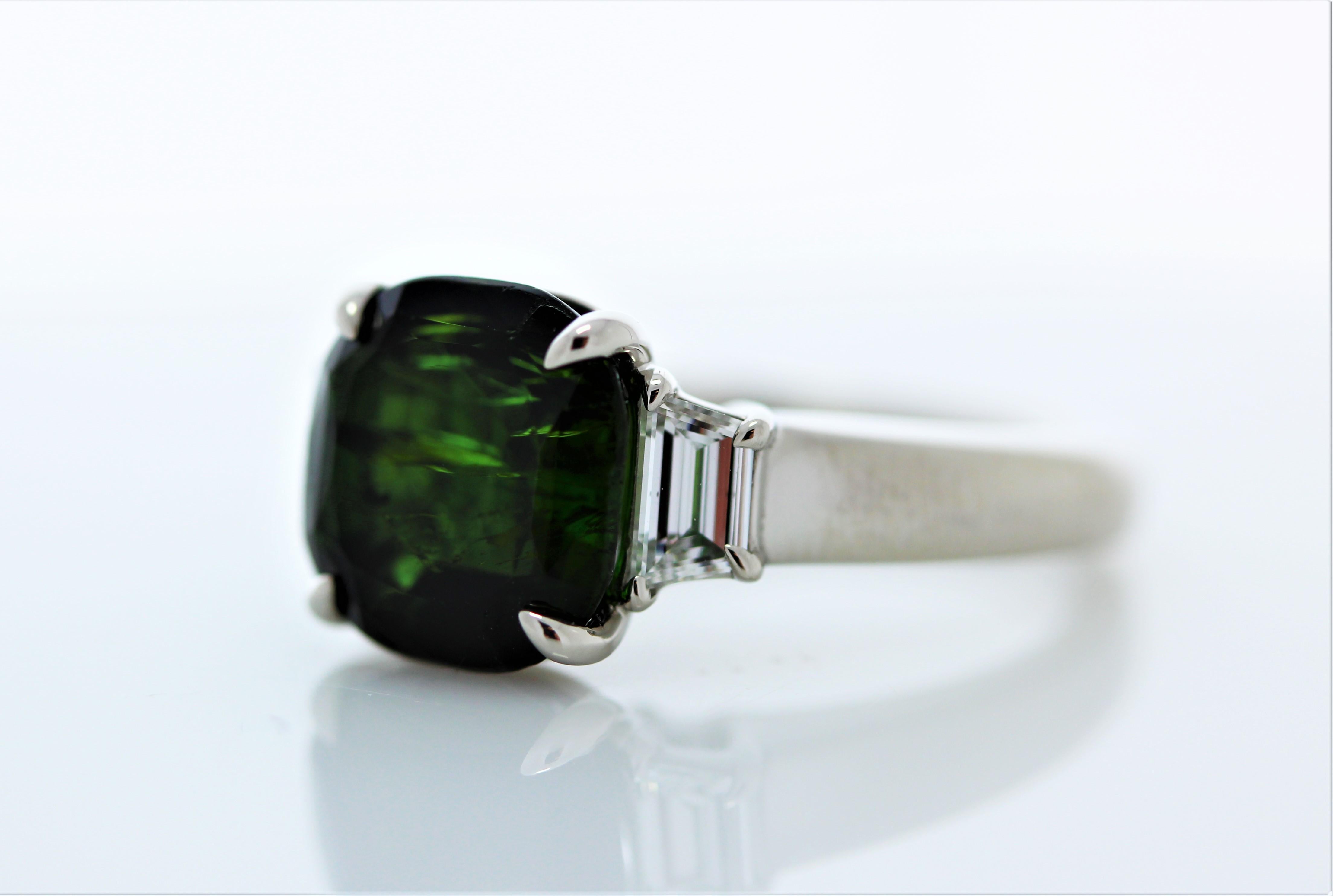 This ravishing green hued tourmaline ring is an incredible sight to behold! The ring features a dynamic 4.56carat tourmaline gemstone. On either side of the gemstone, sit perfectly matched trapezoid cut diamonds that total 0.51 carats. This ring is