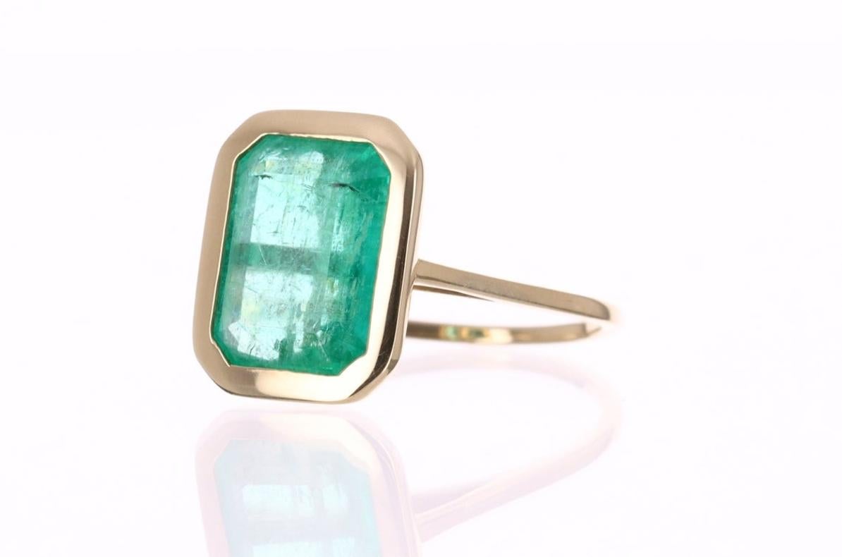 When simple, meets elegant! a beautiful 4.50-carat natural Colombian emerald, with a medium green color and very good luster, is set in a bezel set setting. The setting is very unique, it is in 14K yellow gold, and has diamond accents under the