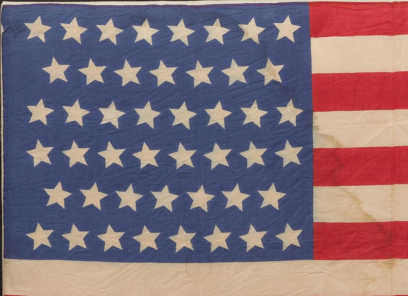 Dies ist eine originale amerikanische Paradeflagge mit 46 Sternen, gedruckt auf Seide. Jeder Stern steht für einen Staat, der zu dieser Zeit zur Union gehörte. Das offizielle Flaggendesign würde jedes Jahr am 4. Juli aktualisiert, um alle neuen