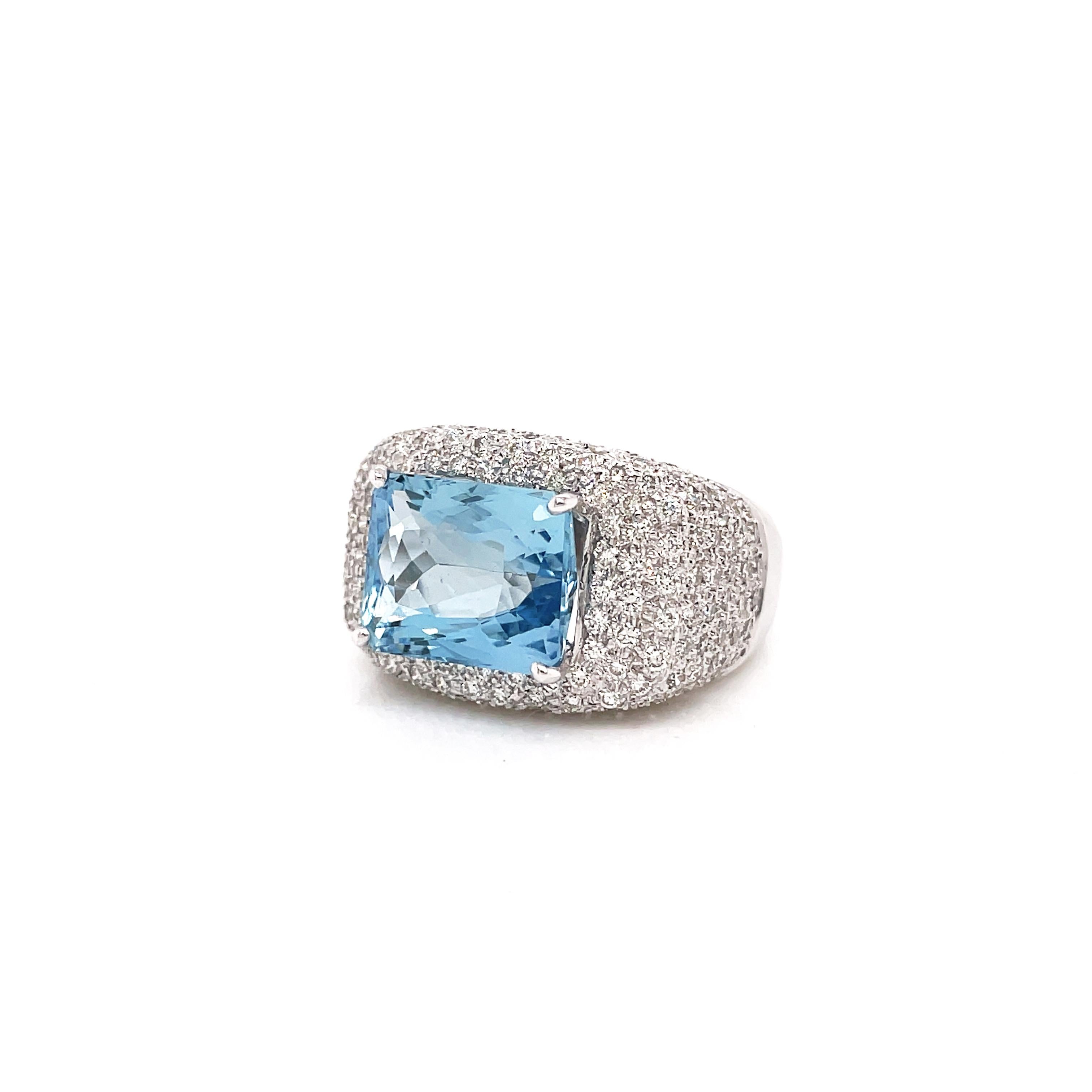 This gorgeous ring features a rectangular cushion cut aquamarine weighing 4.60 carats mounted in a four claw, open back setting. The vibrant gemstone is beautifully surrounded by a cluster of round brilliant cut diamonds totalling to an approximate