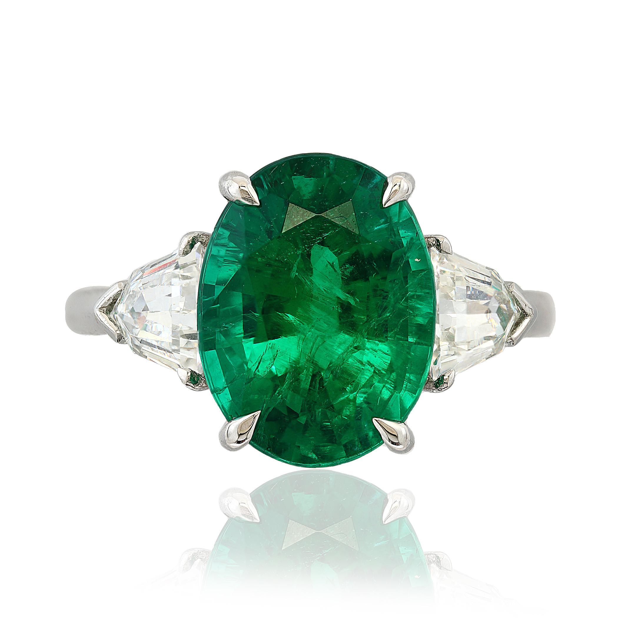 A timeless engagement ring style showcasing a 4.66 carat oval cut  green emerald, flanked by brilliant trillion diamonds on each side. Diamonds weigh 0.90 carats total. Made in platinum.