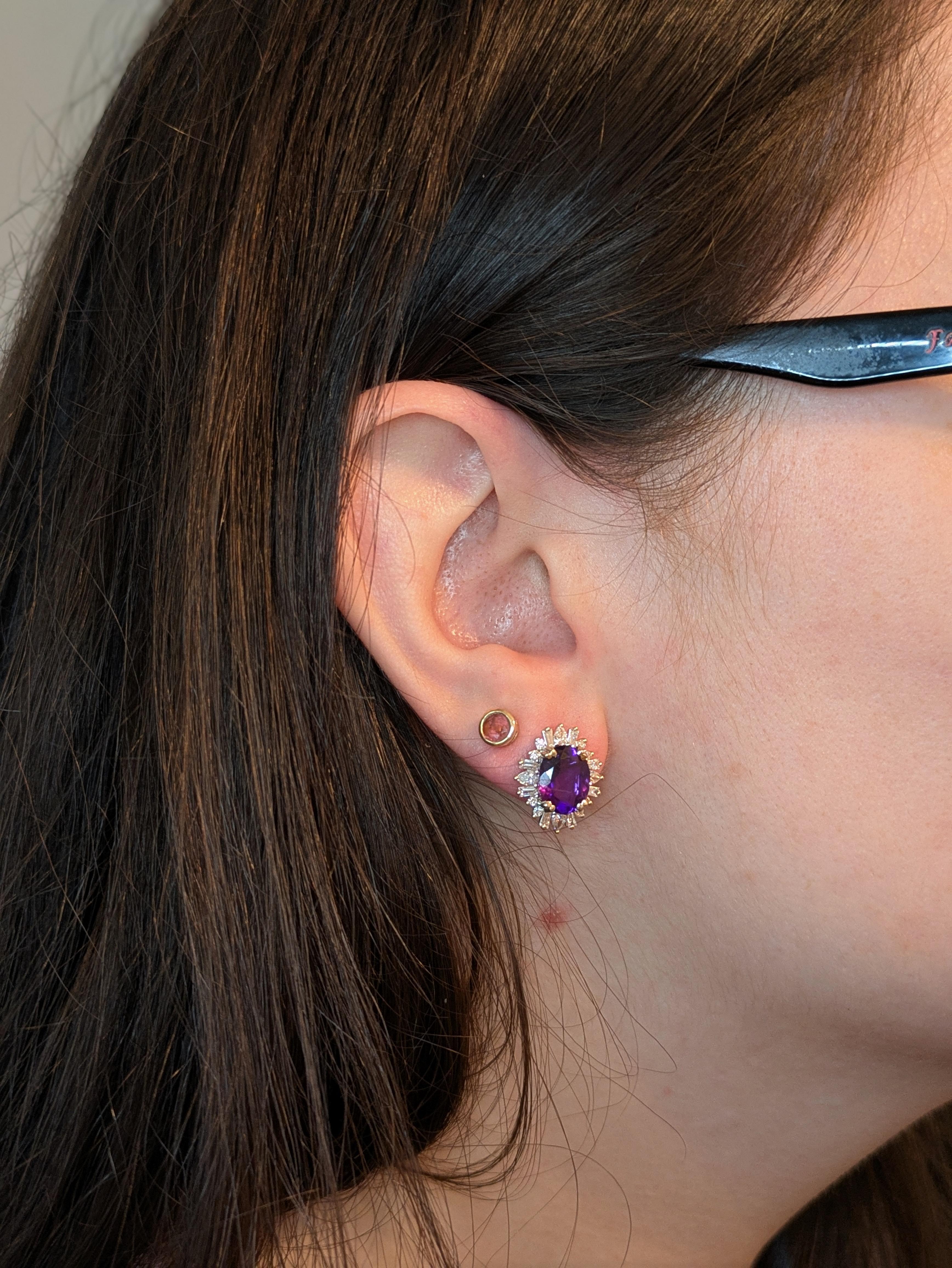 Diese 10x8mm großen ovalen 4,61 Karat sambischen Amethyst Ohrstecker sind ein lebhaftes Statement von Farbe und Handwerkskunst. Jeder Ohrring aus massivem 14-karätigem Weißgold wird von einem schillernden Halo aus erdigen Baguette- und runden