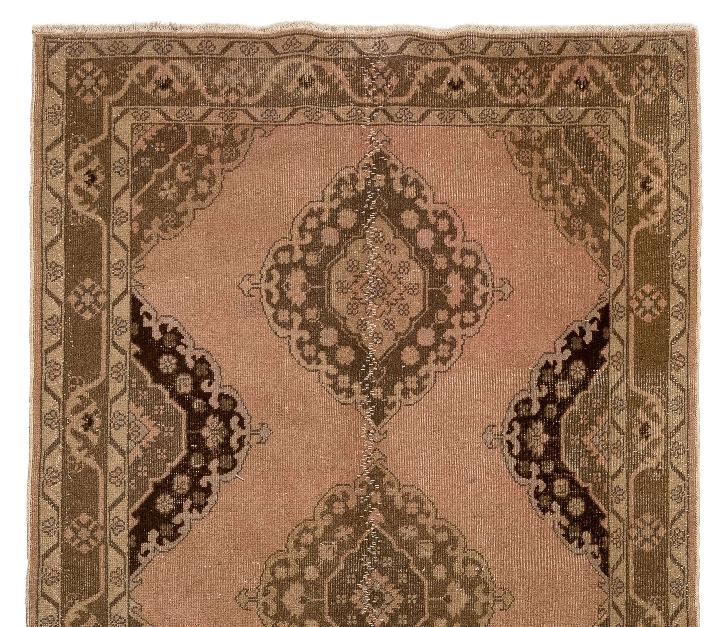 A vintage Turkish runner rug that was hand-knotted in the 1960s with low wool on cotton foundation. It features multiple linked medallions in brown and sand colors against a faded coral pink background. It is in good condition,