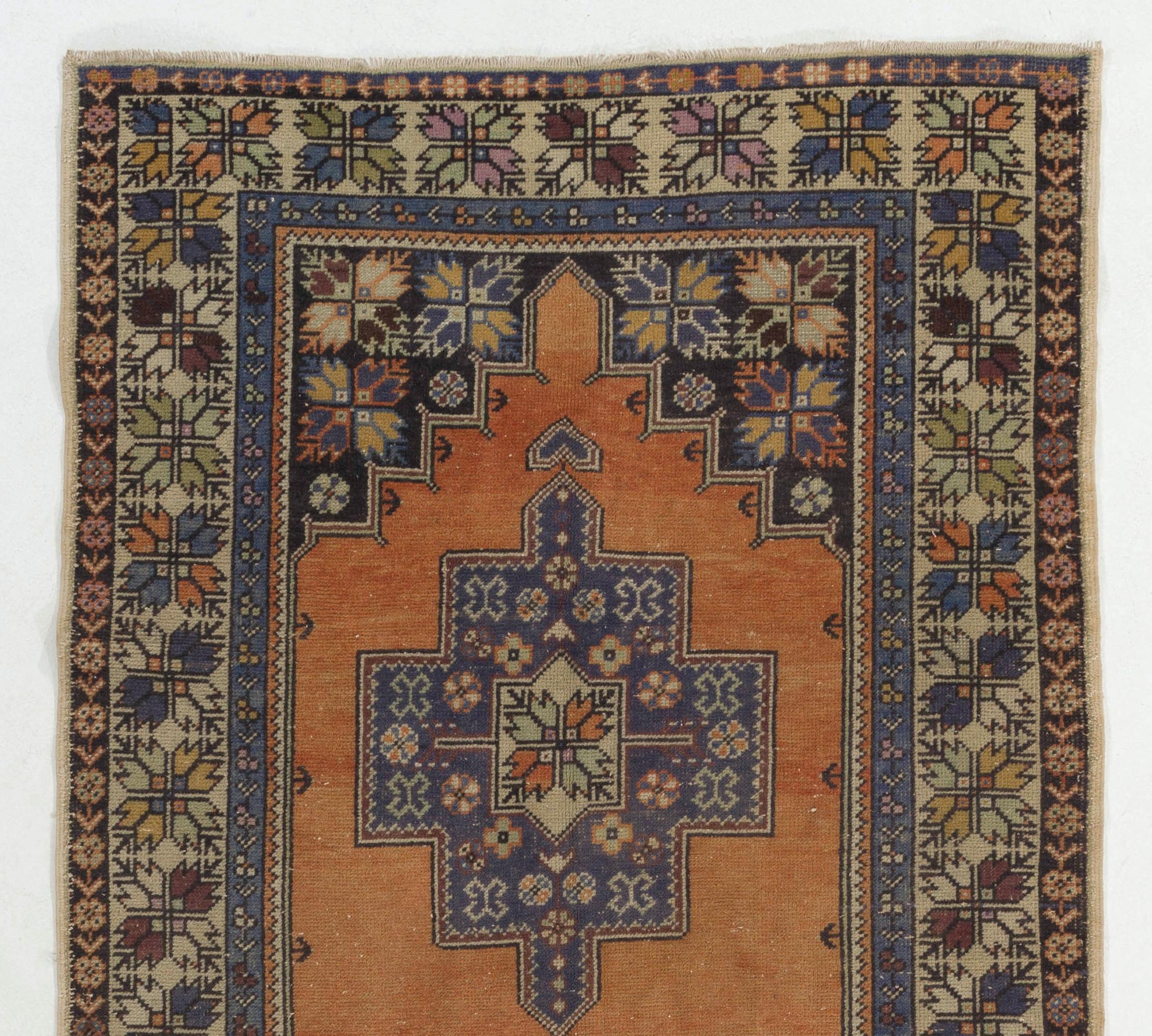 This vintage hand knotted Turkish rug features two linked geometric medallions in cornflower blue decorated with free floating small floral heads and star motifs against a plain field in soft, faded madder red. The corner pieces have a dark, black