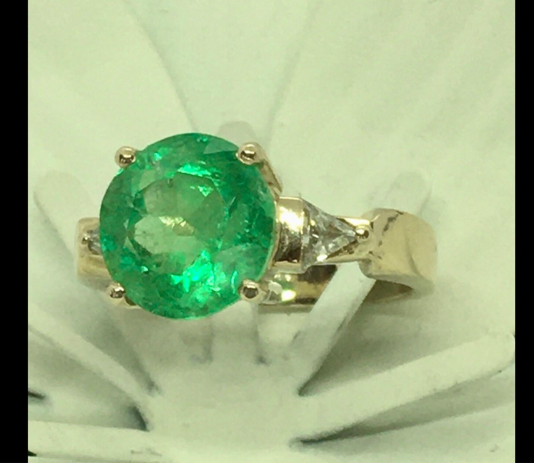 Classic Solitaire Colombian round cut emerald engagement ring diamond accented. 
Center; Fine brilliant natural green Colombian emerald round cut 4.20 carat, measurement 10.40mmX10.40mm. Medium Green/ VS.
Accent Stone: Trillion cut Diamond 0.50