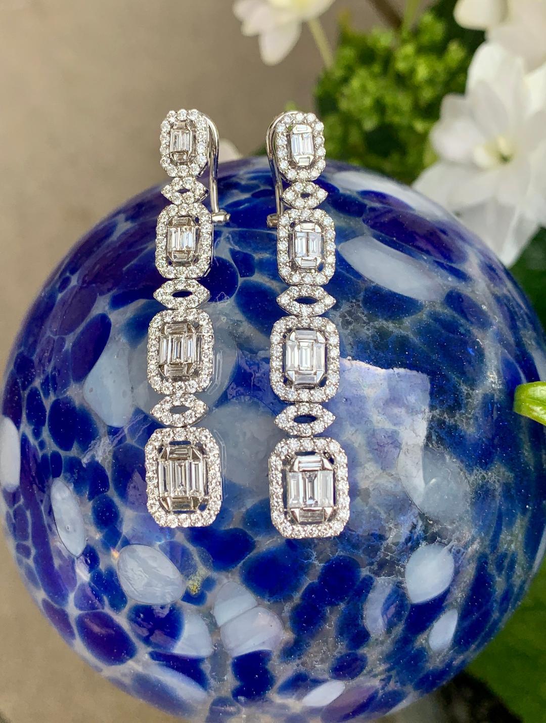 Beautiful pair of 18 karat white gold Art Deco style dangling earrings feature invisibly set baguette diamonds which give the illusion of a very large, cut cornered emerald cut diamond in the center of each tier. Each of the four emerald shaped