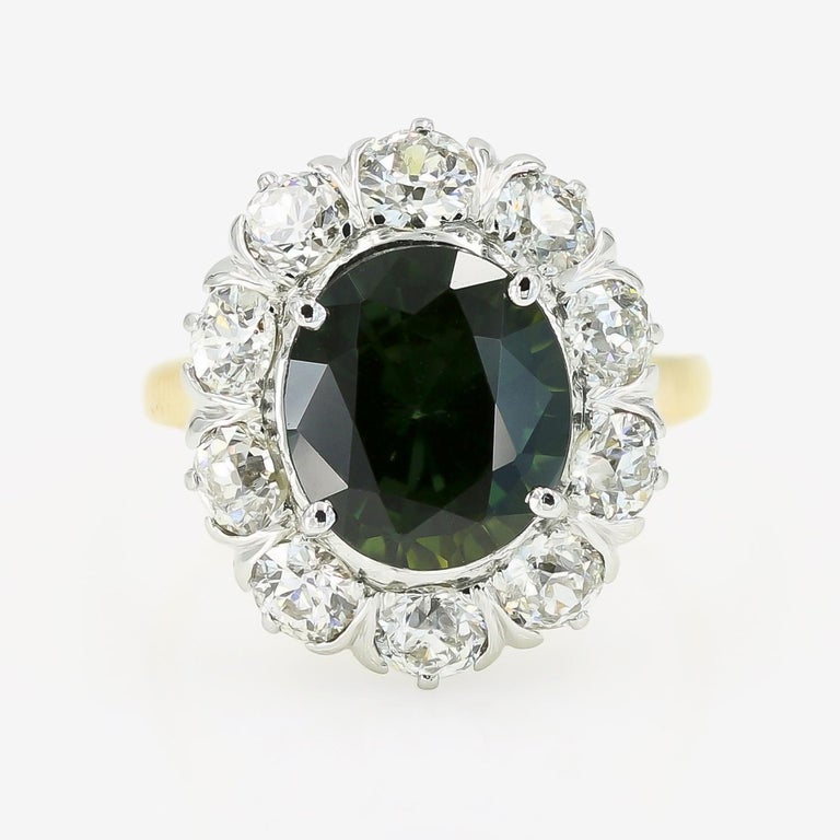 This 14kt. white and yellow gold ring contains a remarkable 4.75cts. oval cut green sapphire center stone. The center is surrounded by 10 old mine cut diamonds approximately 1.80cts. t.w. The diamonds are H-I in color and SI-I1 in clarity. The