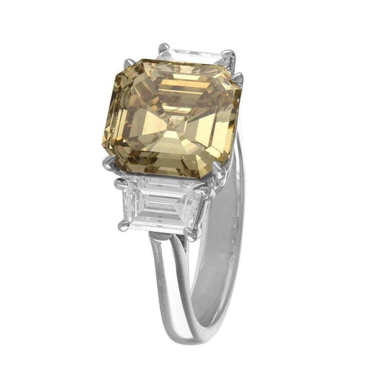 4.76 Carat Square Emerald Cut Diamond is set in a Three Stone Platinum & 18K Yellow Gold Ring. The Square Emerald is Certified as Fancy Deep Brownish Yellow in Color and SI1 in Clarity.  On the Sides of the Center there are Two Step Cut Trapezoids.