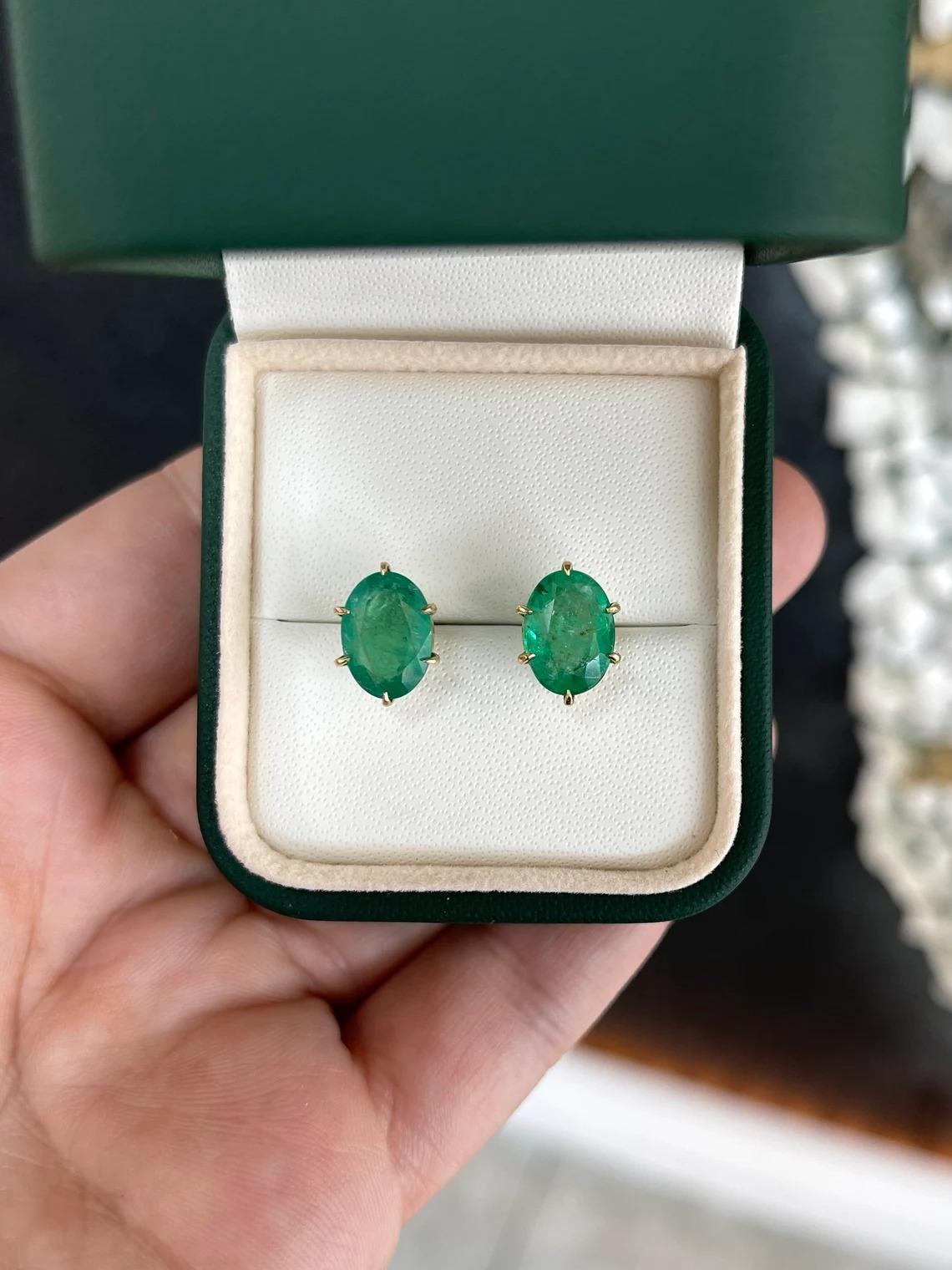 Featured here is a six-prong, solitaire, oval-cut emerald studs in fine 18K yellow gold. Displayed are gorgeous, medium green emeralds with incredible size and high quality that make these so ideal for an emerald lover. The gems are accented by
