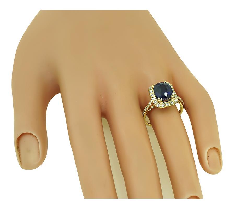 Este es un precioso anillo de compromiso de oro amarillo de 14k. En el centro del anillo hay un precioso zafiro de Ceilán talla cojín que pesa aproximadamente 4.79 ct. El zafiro está acentuado por brillantes diamantes de talla redonda que pesan