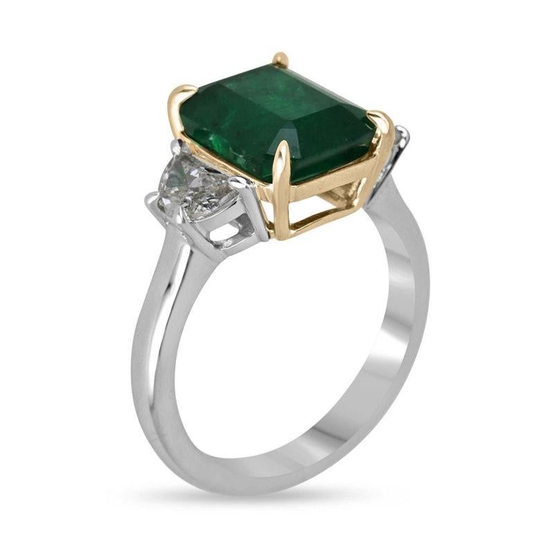Introducing our exquisite three-stone ring, boasting a magnificent 4.16-carat emerald, radiating pure emerald galore. This triple-A quality gem, with its rich, dark green hue, captivates with its profound emerald cut and stunning facets. Set in a