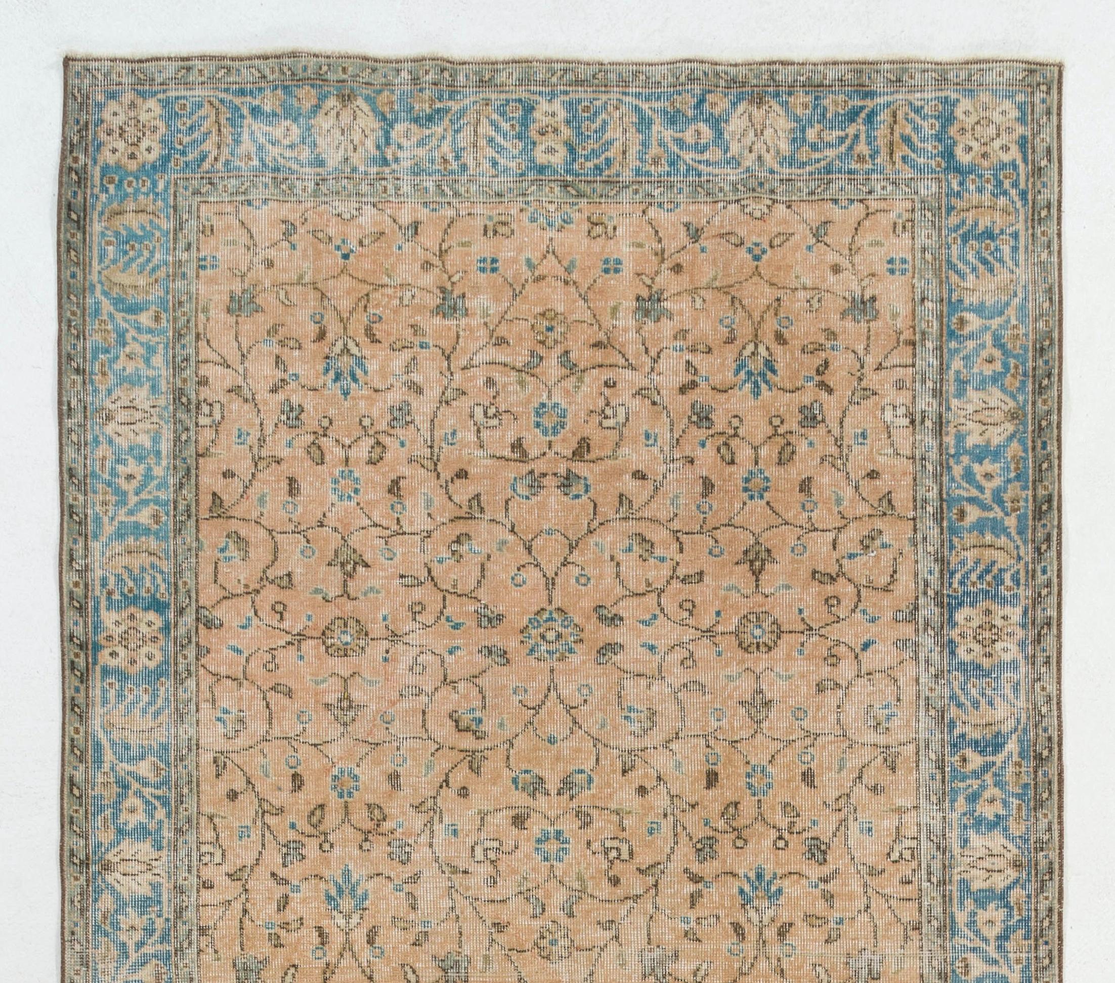 A vintage hand-knotted runner rug from Central Turkey with an all-over design of scrolling floral and leafy vines against a coral pink background and a border in faded blue decorated with palmettes, rosettes and serrated leaves. 

The rug has low