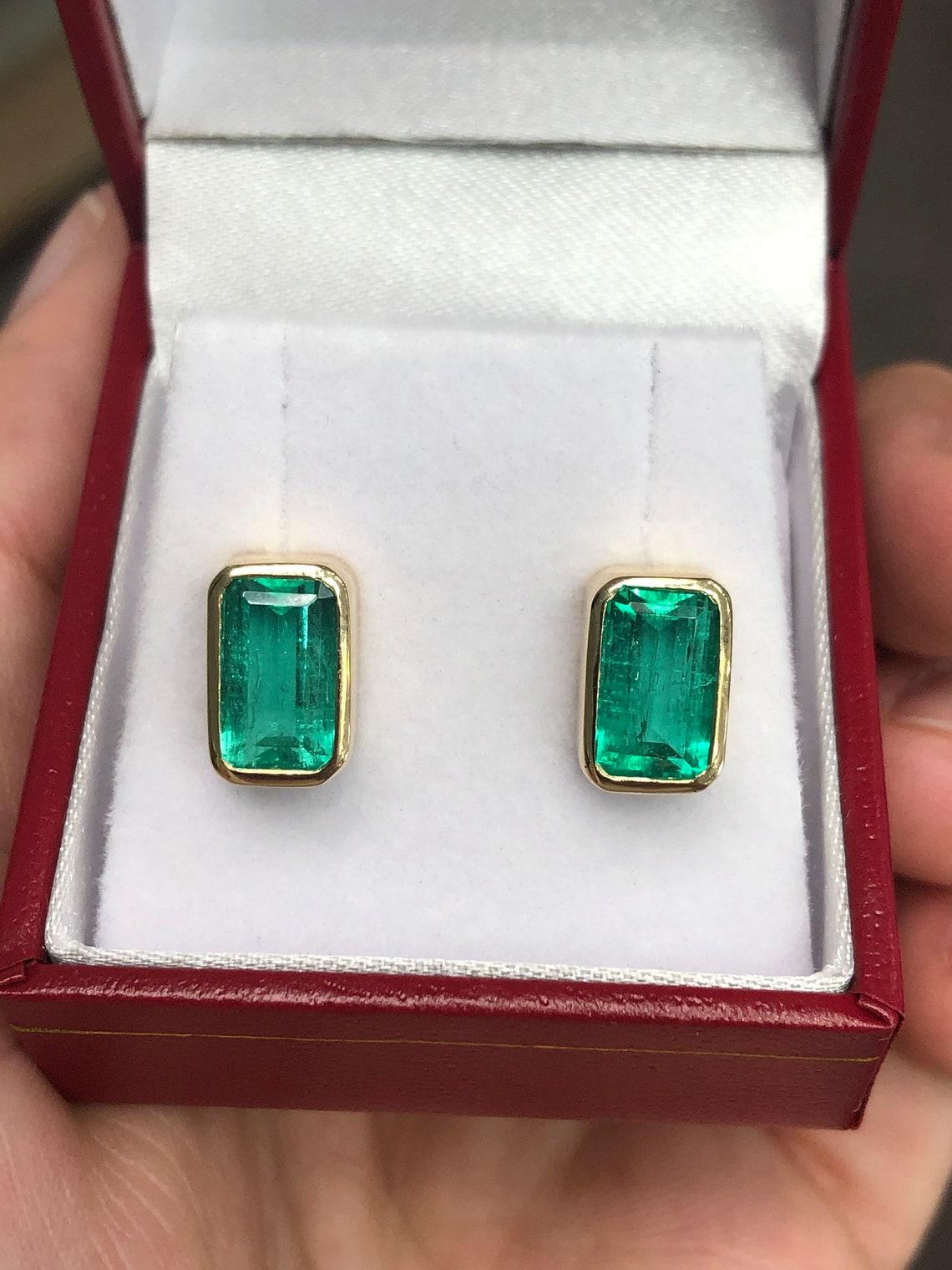 These VS 4.86tcw earrings are not for the faint of heart! Featured here is a stunning set of emerald-cut Colombian emerald studs in fine 14K yellow gold. Displayed are lustrous, green emeralds with incredible transparency, accented by a handmade