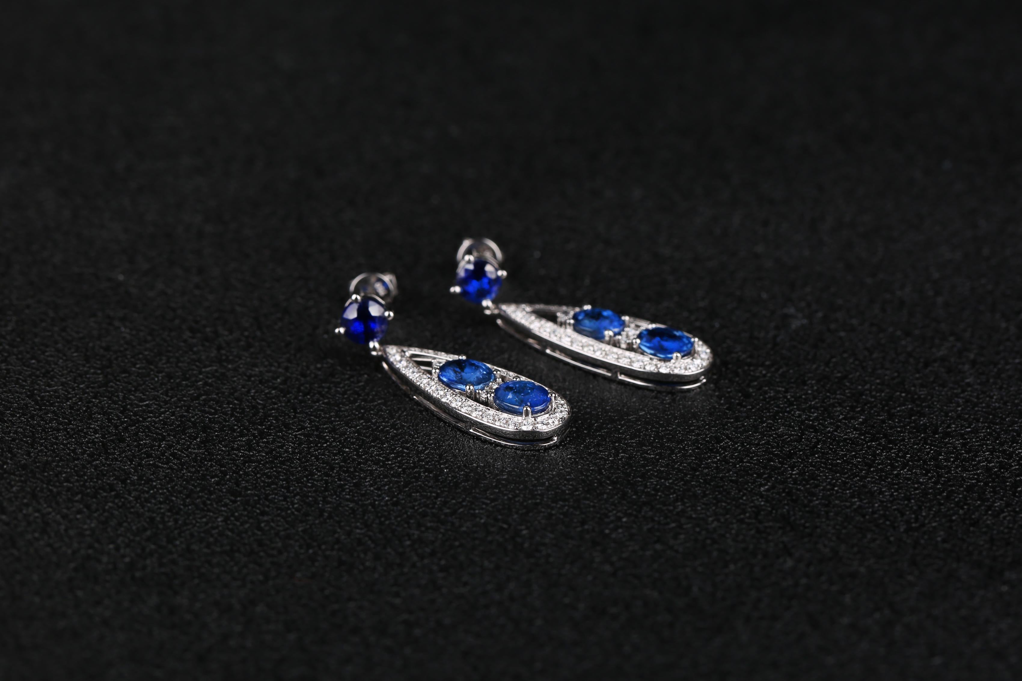A Pair of Sapphire dangle drop earring in 18K White Gold. The elongated rain drop is suspended below a Sapphire ear stud. There are 2 sapphire sitting in each side of the rain drop and they are surrounded by diamond pave. It is a very contemporary