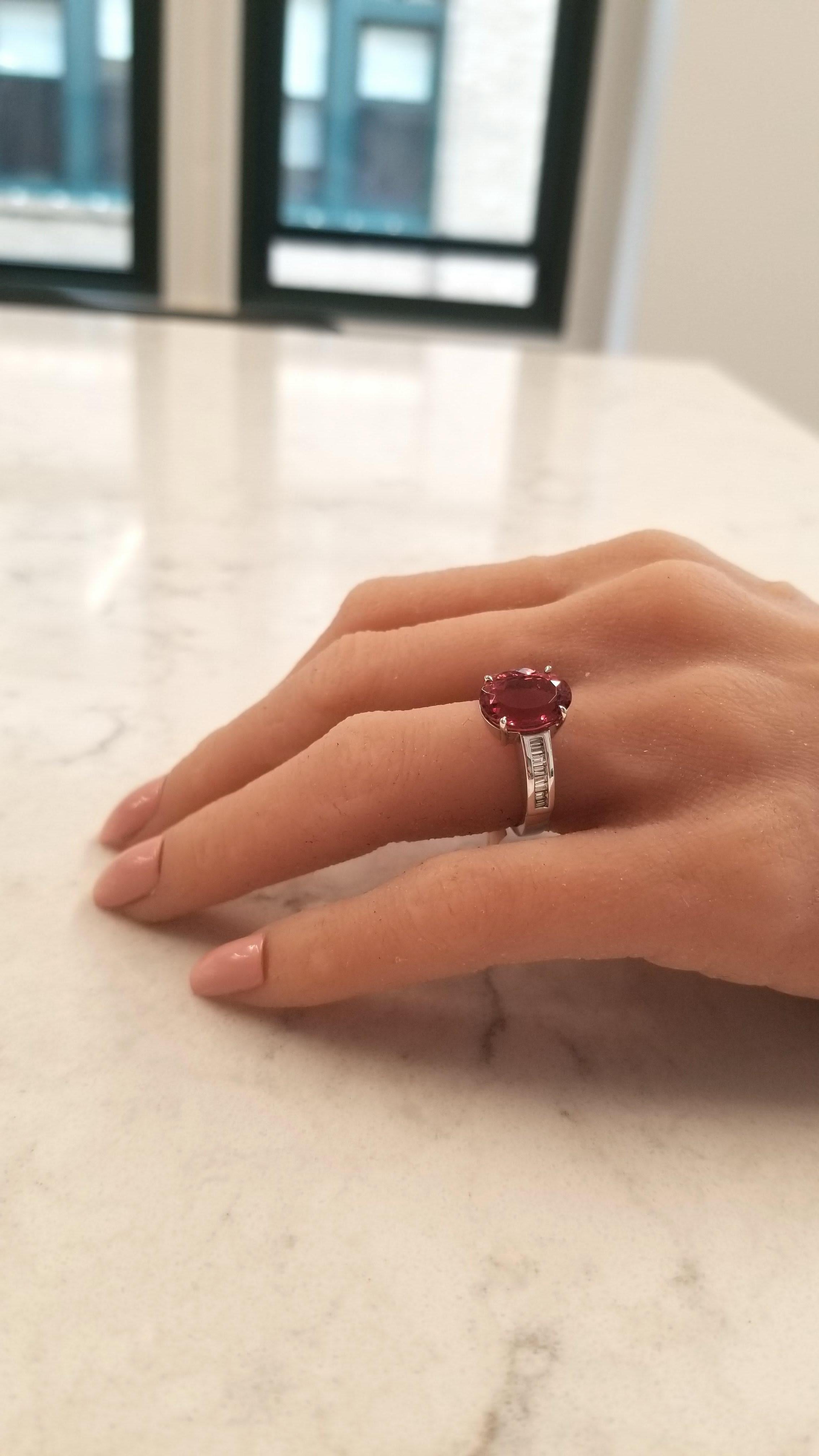 Created in brightly polished 14 karat white gold, this beautiful custom made engagement anniversary ring features one vibrant raspberry rubellite tourmaline prong-set in the center, accented by shimmering baguette cut diamonds that are invisibly