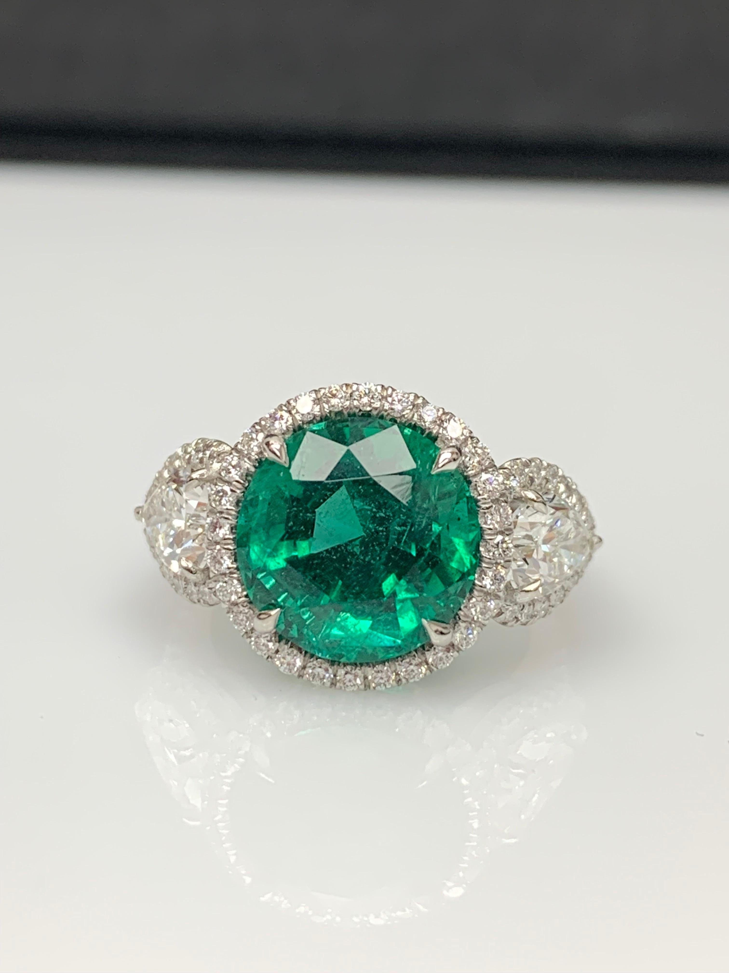 Une superbe bague mettant en valeur une riche et intense émeraude de taille ronde et brillante pesant 4,95 carats, entourée d'une rangée de diamants. La pierre centrale est flanquée de deux diamants en forme de poire, d'un poids total de 1,40 carat,