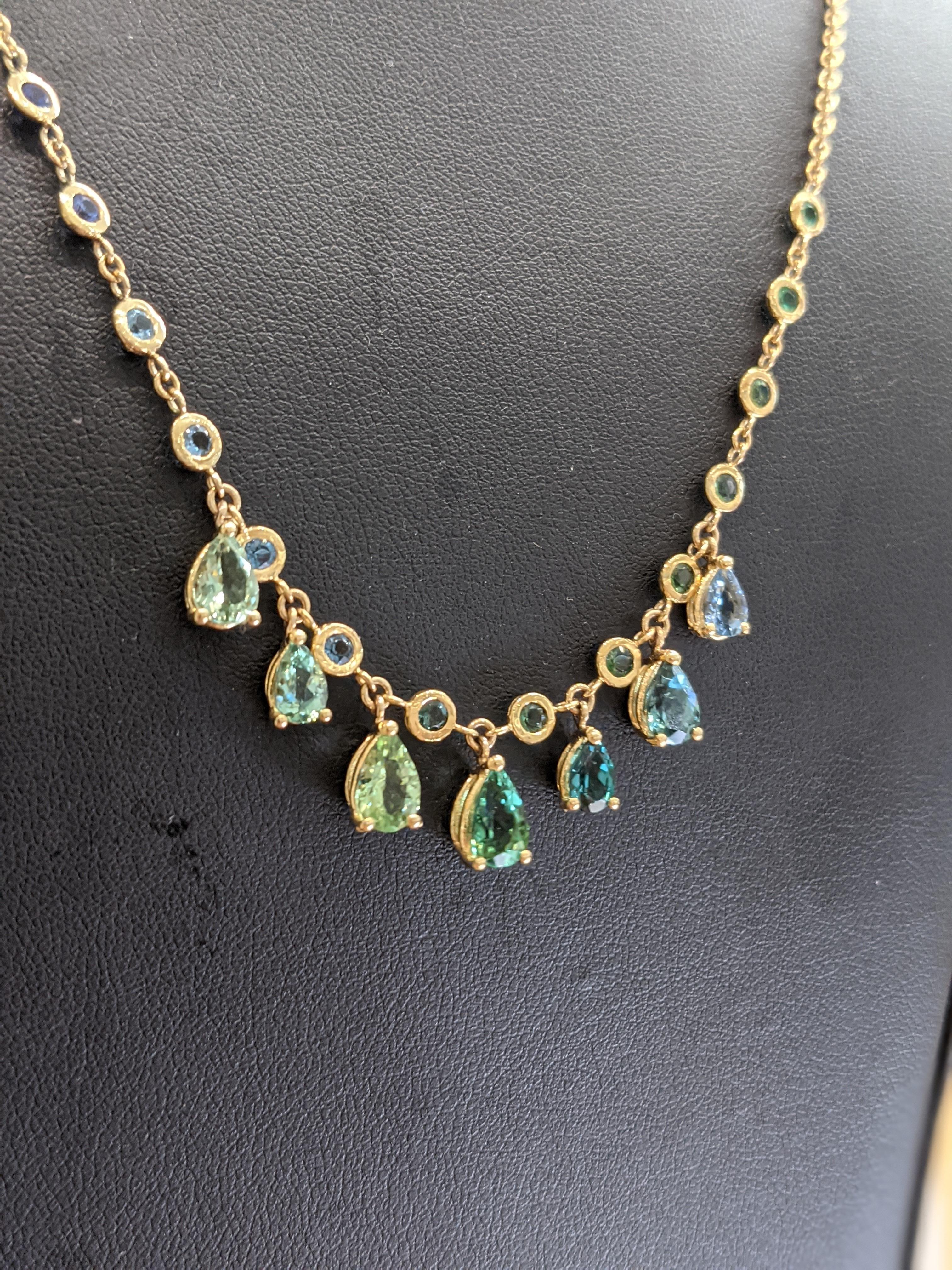 Elevate your style with this unique 18k yellow gold necklace, 4.95 carat weight of a combination of different, natural gemstones, pear shape cut, alternated by round bezeled Aquamarine and Emeralds.
The array's selection consists of different color
