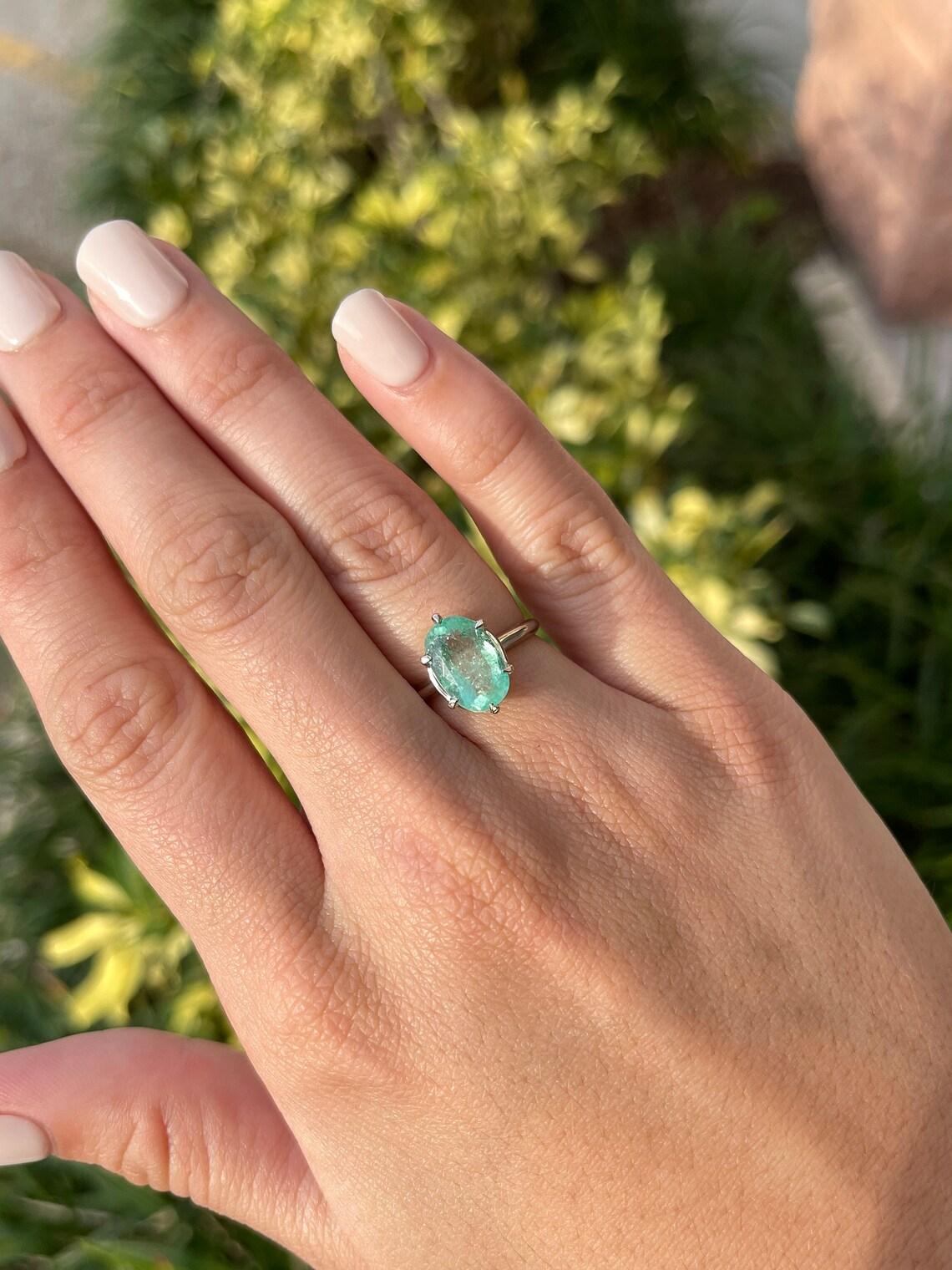 A light green Colombian emerald solitaire ring in 14k white gold. This natural emerald comes from the beloved mines of Colombia and showcases a pastel green color that enthralls at each glance. The emerald has natural imperfections which are a key