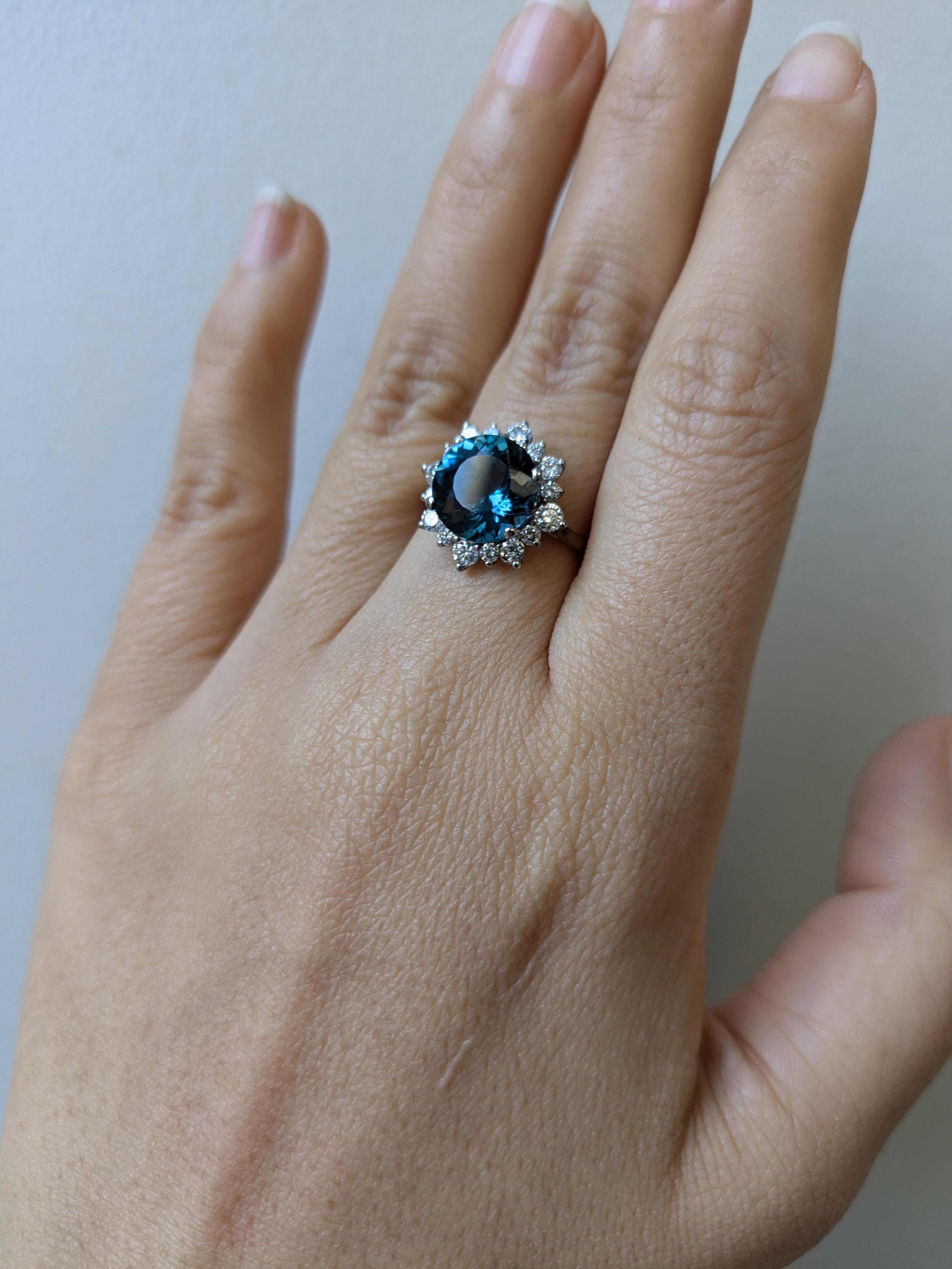 Inspirée par les fleurs épanouies, cette bague en or véritable 14 carats présente en son centre une topaze bleue de Londres de 4,05 carats, entourée d'un halo de diamants rayonnants. Des diamants minés par la terre et de délicats détails floraux