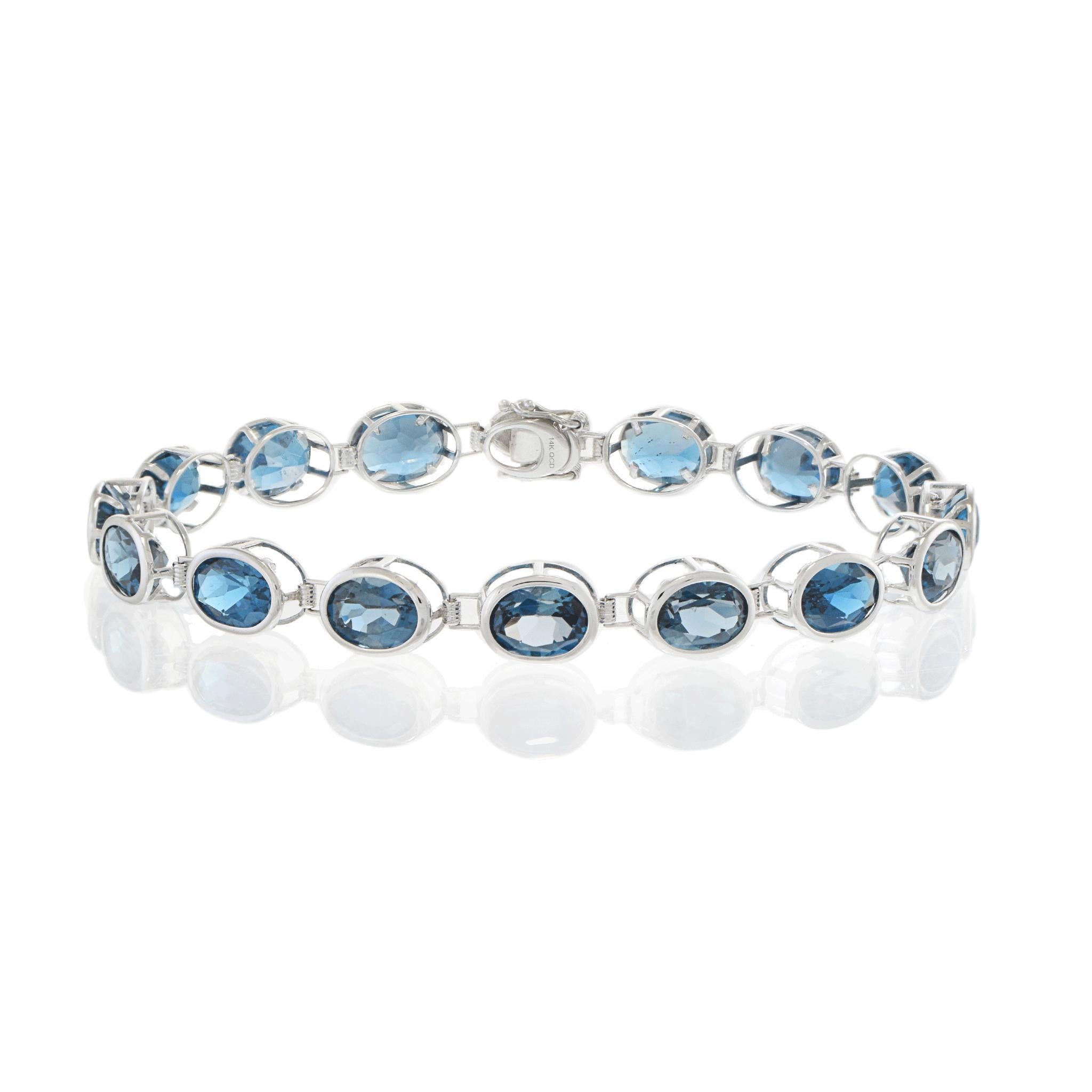D'une teinte éclatante et d'un design sophistiqué, ce bracelet en or blanc 14KT présente une rangée continue de pierres précieuses ovales en topaze bleue de Londres serties sur un chaton, totalisant un impressionnant total de 21,87 carats. Chaque