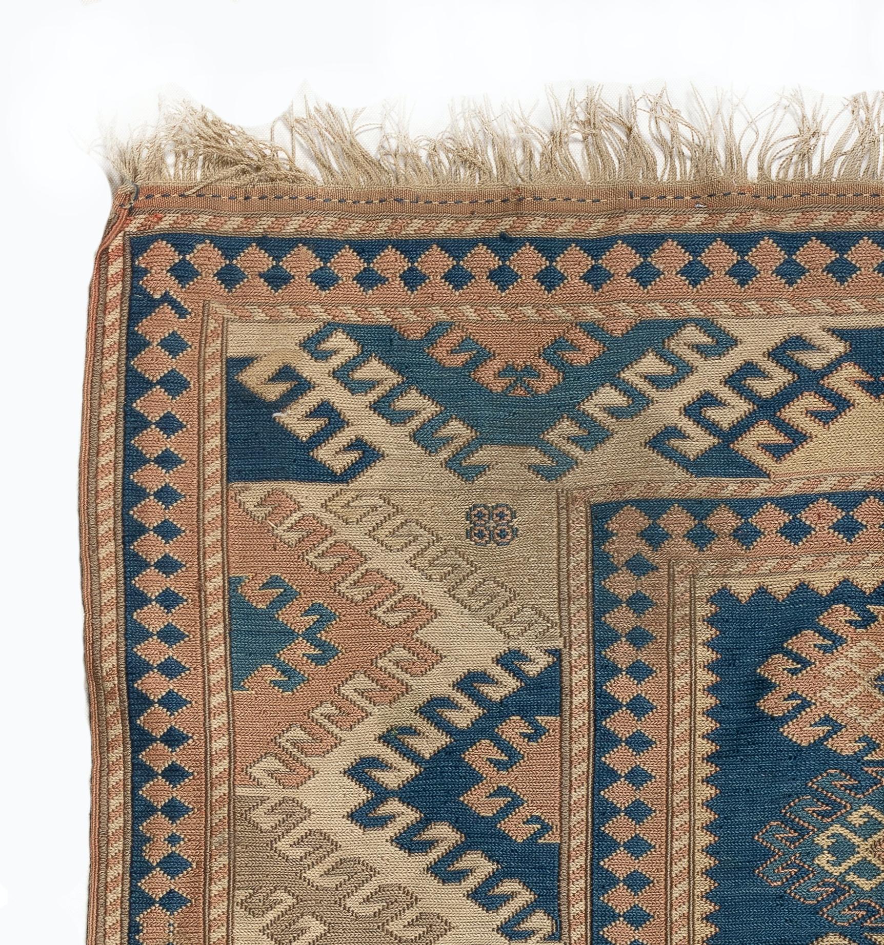 A vintage Turkish carpet from the 1960s featuring a geometric design with linked latch hook medallions at its centre and a very large border decorated all over with bigger half latch-hook medallions, all in navy blue, pale terra cotta red and sand