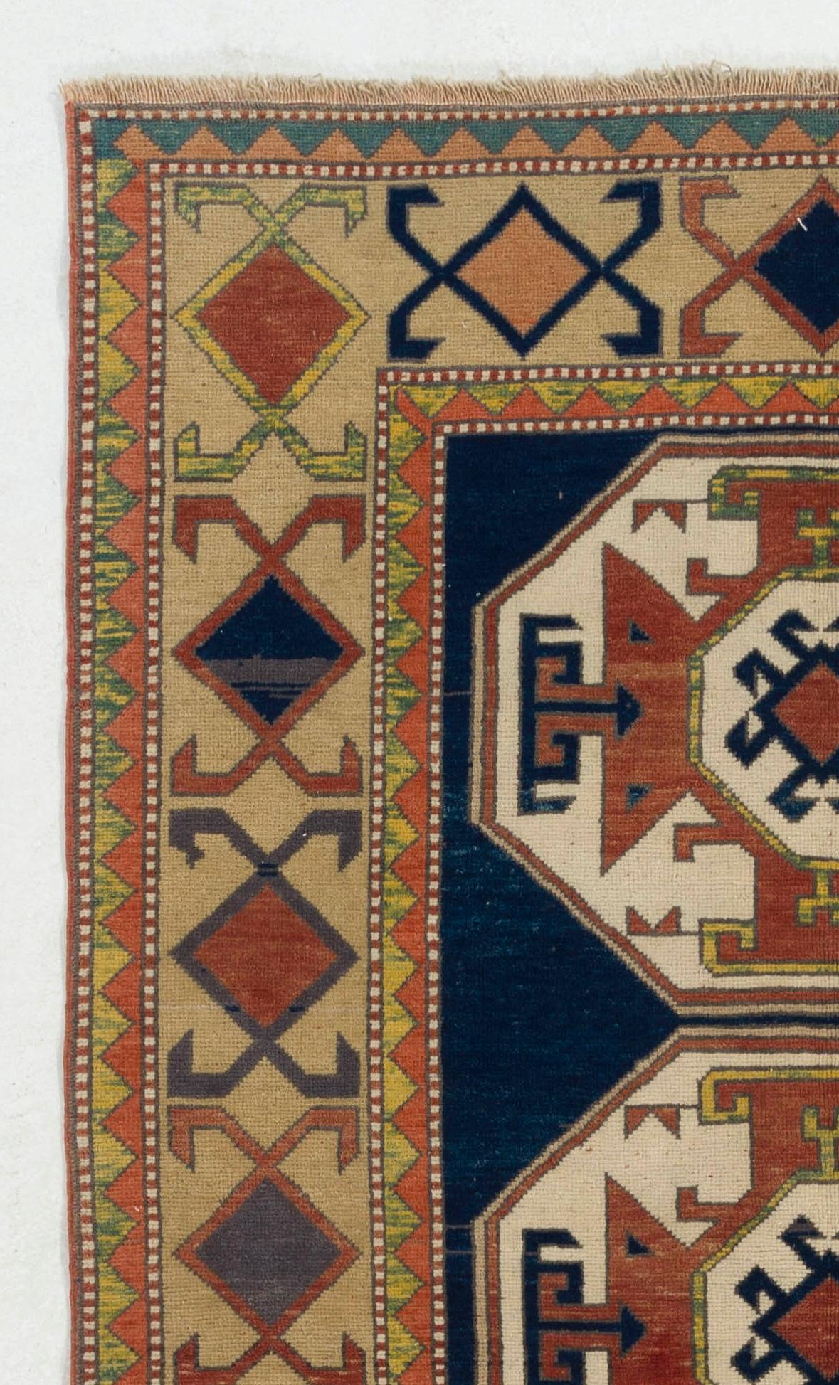 Ce tapis Kazak vintage présente deux médaillons en forme de croix reliés entre eux, d'un rouge garance et d'un beige doux, sur un champ indigo foncé et profond, orné de motifs quadrilobés flottant librement. La bordure principale, remplie de têtes