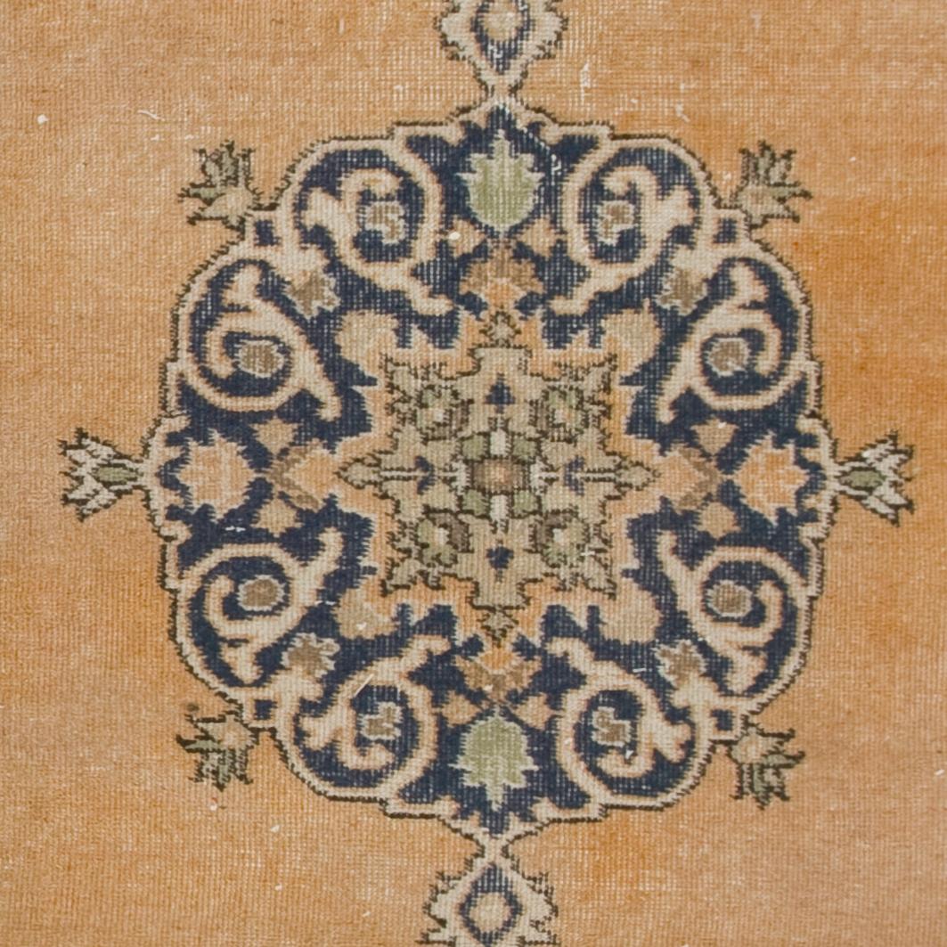 Un tappeto vintage proveniente dalla Turchia centrale, finemente annodato a mano con un vello di lana di media grandezza su una base di cotone. Presenta un classico disegno a medaglione in indaco su un campo arancione tenue, incorniciato da angoli