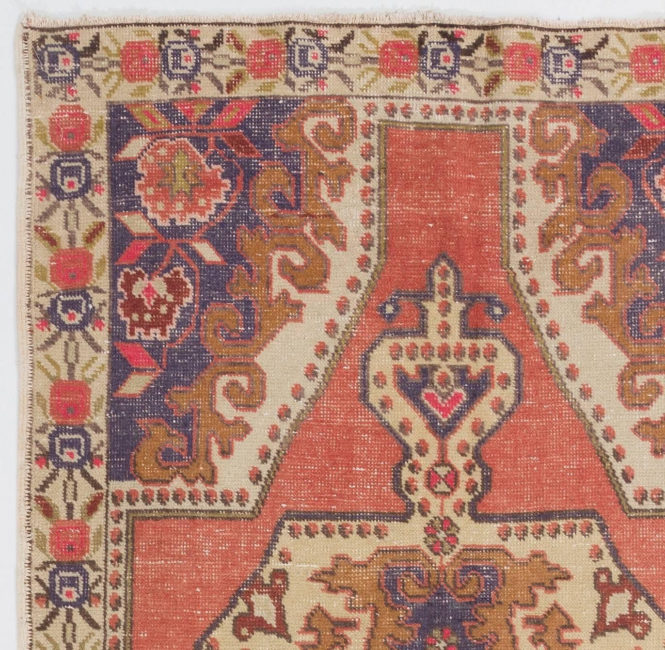 A vintage village rug from Turkey. It is made of medium wool pile on wool foundation and features a large medallion at its center, floral corner pieces and a floral main border in dark blue, light brown and grass green against a rich coral pink and