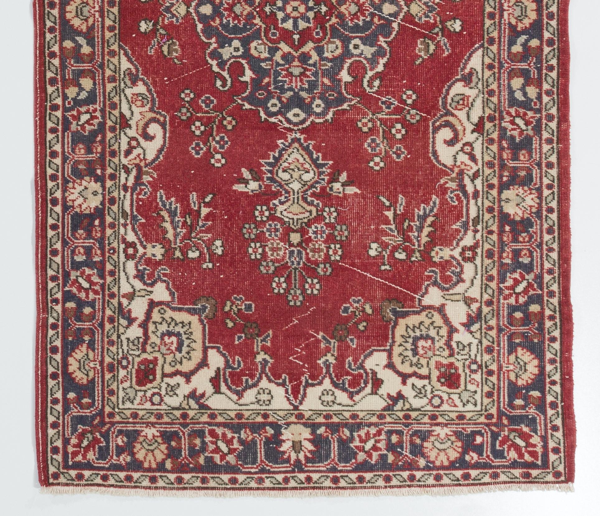 This vintage hand knotted Turkish area rug was originally made in the 1960s. It features a central medallion in faded navy blue, flanked on either side by two vases holding bouquets of dainty blossoms in a carmine red field decorated with more