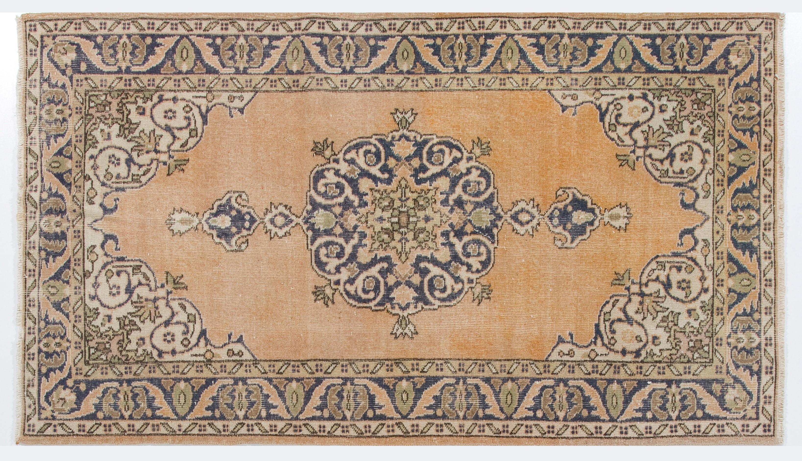 A vintage Turkish Oushak area rug with a central tear-drop medallion in dark indigo blue against a plain field in faded peach with arabesque corner-pieces. The rug is finely hand-knotted and has low wool pile on cotton foundation. It is deep-washed,