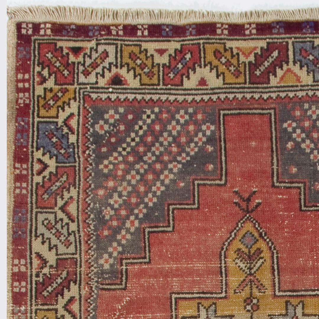 Esta alfombra vintage de Anatolia Central presenta dos medallones enlazados en dorado saturado con motivos en forma de cruz en su interior sobre un campo liso en rojo suave apagado. Los esquineros en gris marengo están decorados con grandes palmetas