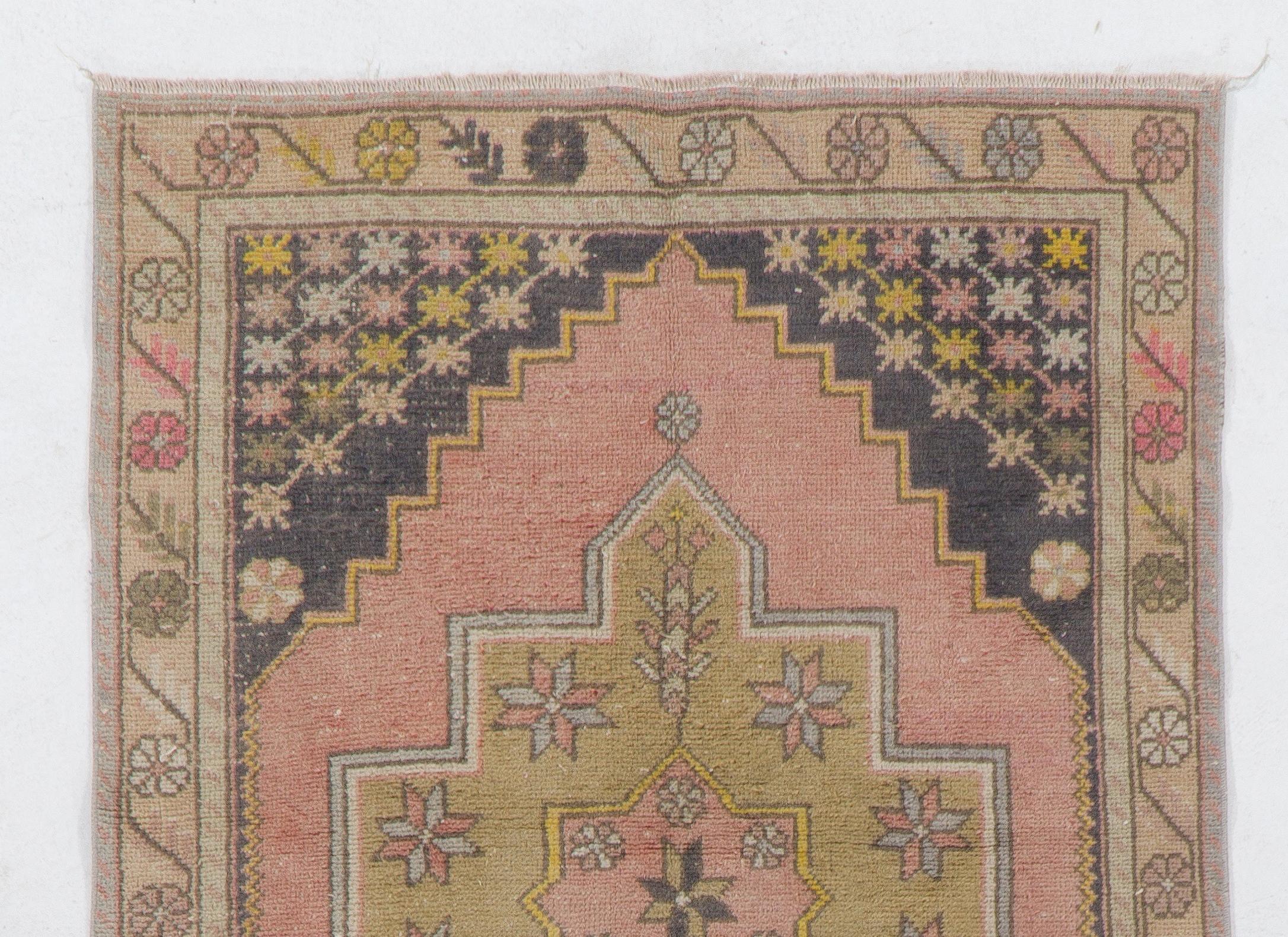 This vintage area rug was hand-knotted in Turkey in the 1950s. It features a geometric medallion at the centre of two nested lozenge-shaped areas within a field in faded red and faded black colors featuring tassel-like motifs on their borders. The