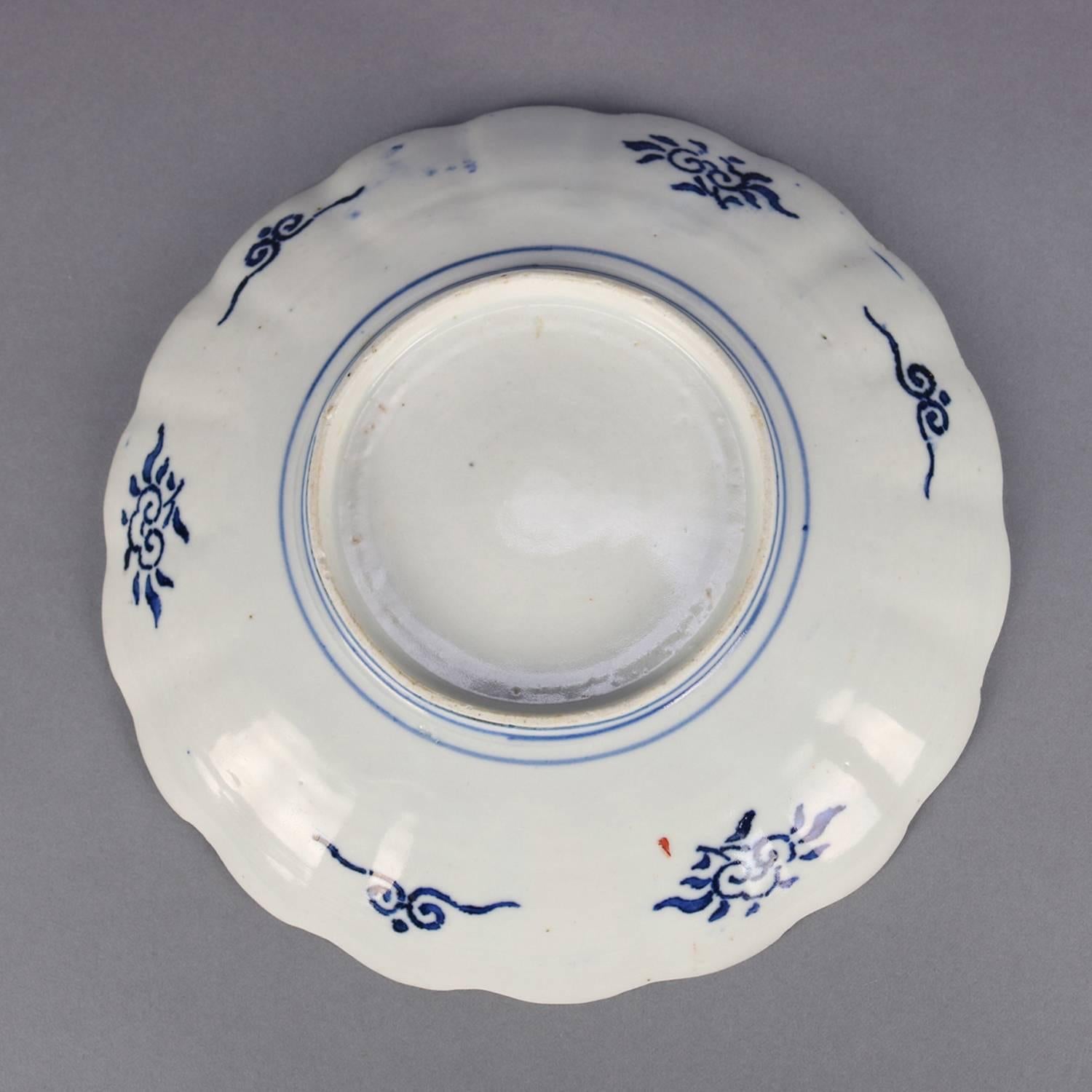 Five Antique Japanese Meiji Imari porcelain features plates with scalloped rims with alternating hand-painted reserves of garden, floral and stylized fish scales surrounding central reserve of urn with flowers, en verso blue decoration; set includes
