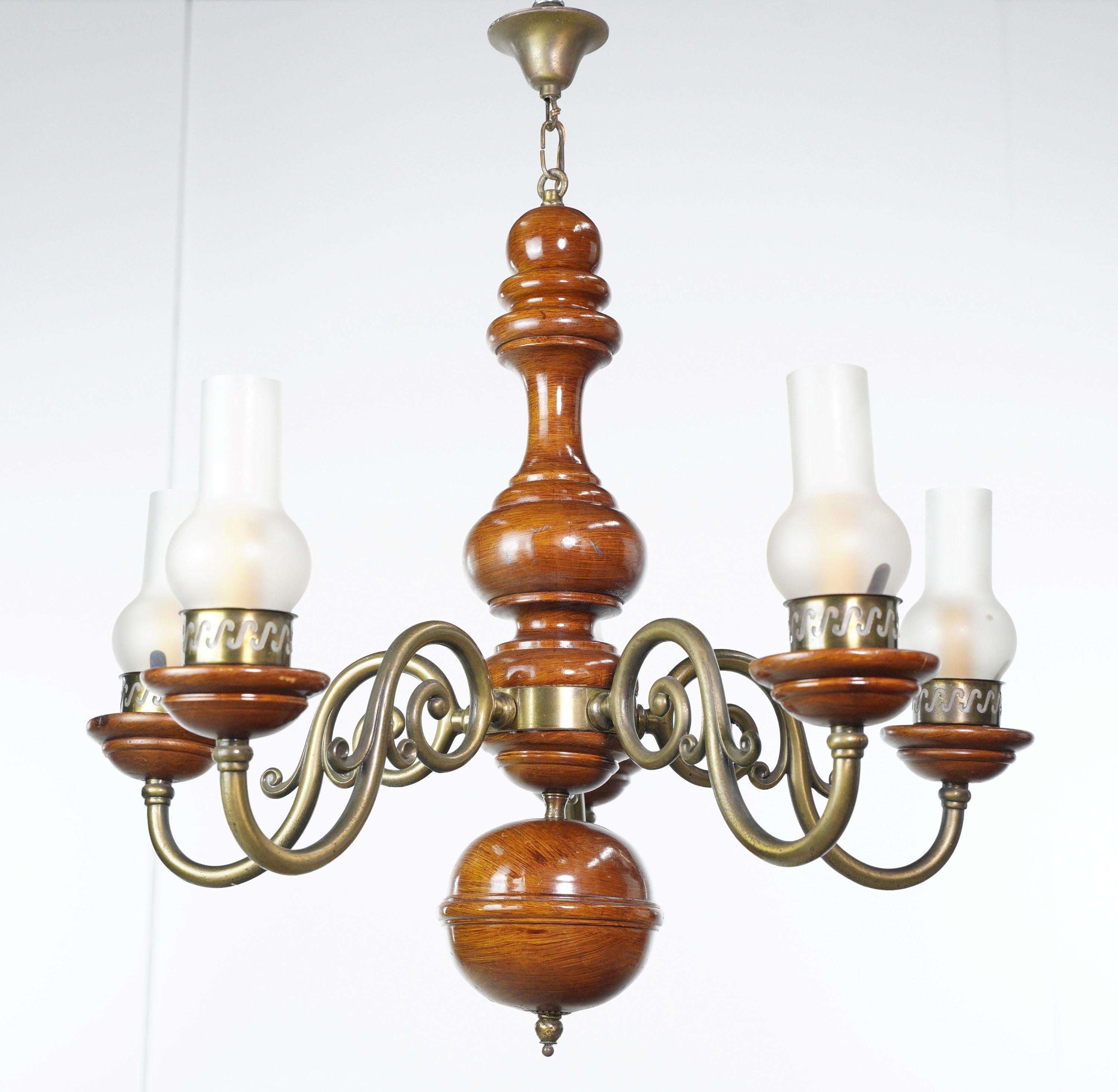 This Traditional five arm wooden chandelier is a classic lighting piece, blending the warmth of medium-tone wood with the timeless elegance of brass-plated arms with hurricane glass shades, creating a charming focal point in any traditional setting.